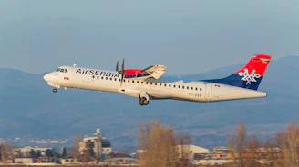 Air serbia turboprop airplane taking off with mountains behind.