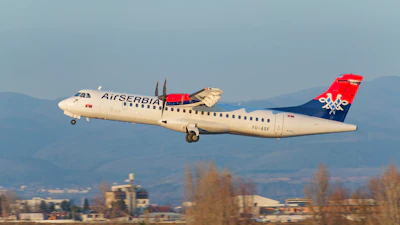 Air serbia turboprop airplane taking off with mountains behind.