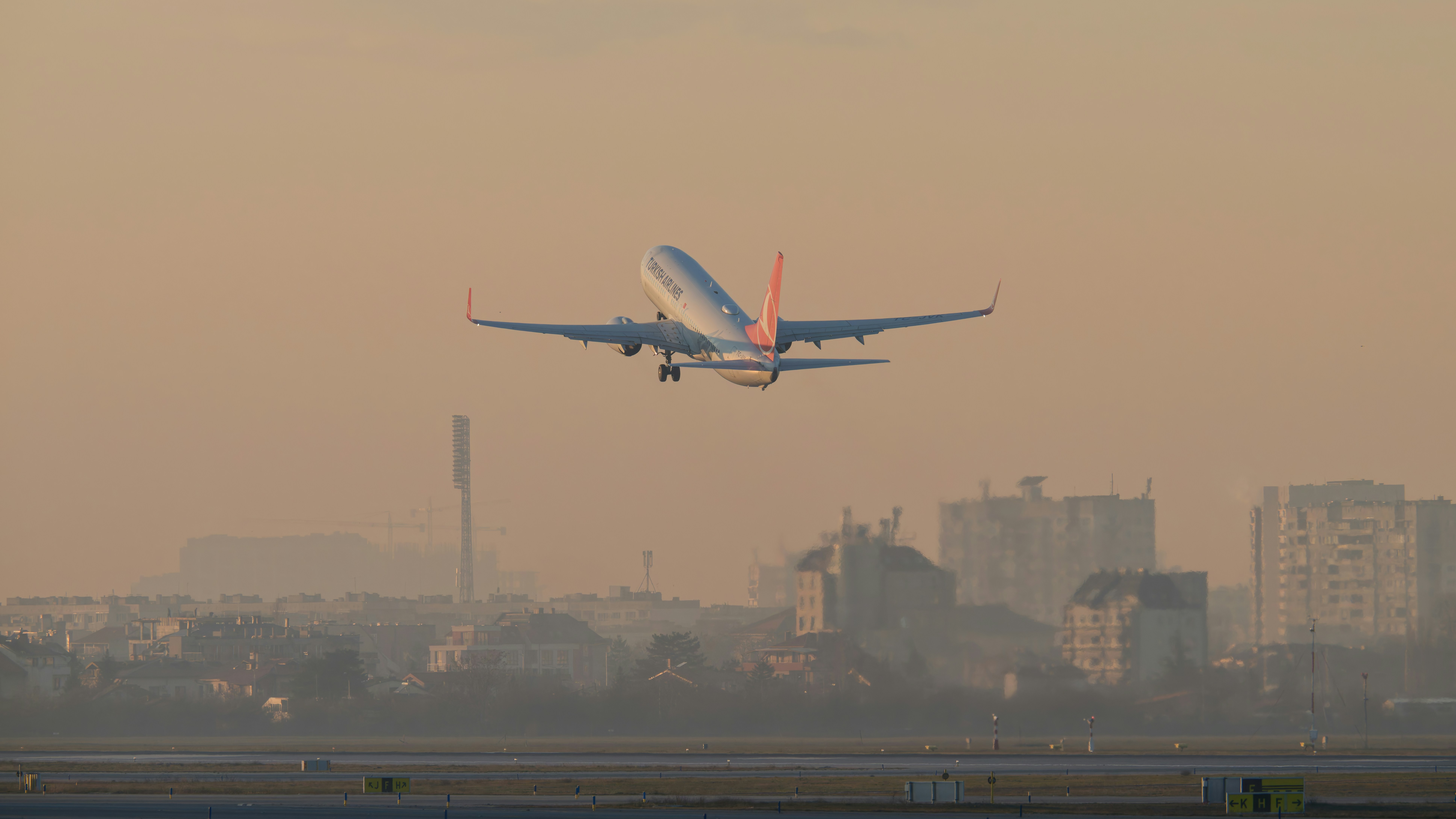 Airplane taking off over city buildings at sunset