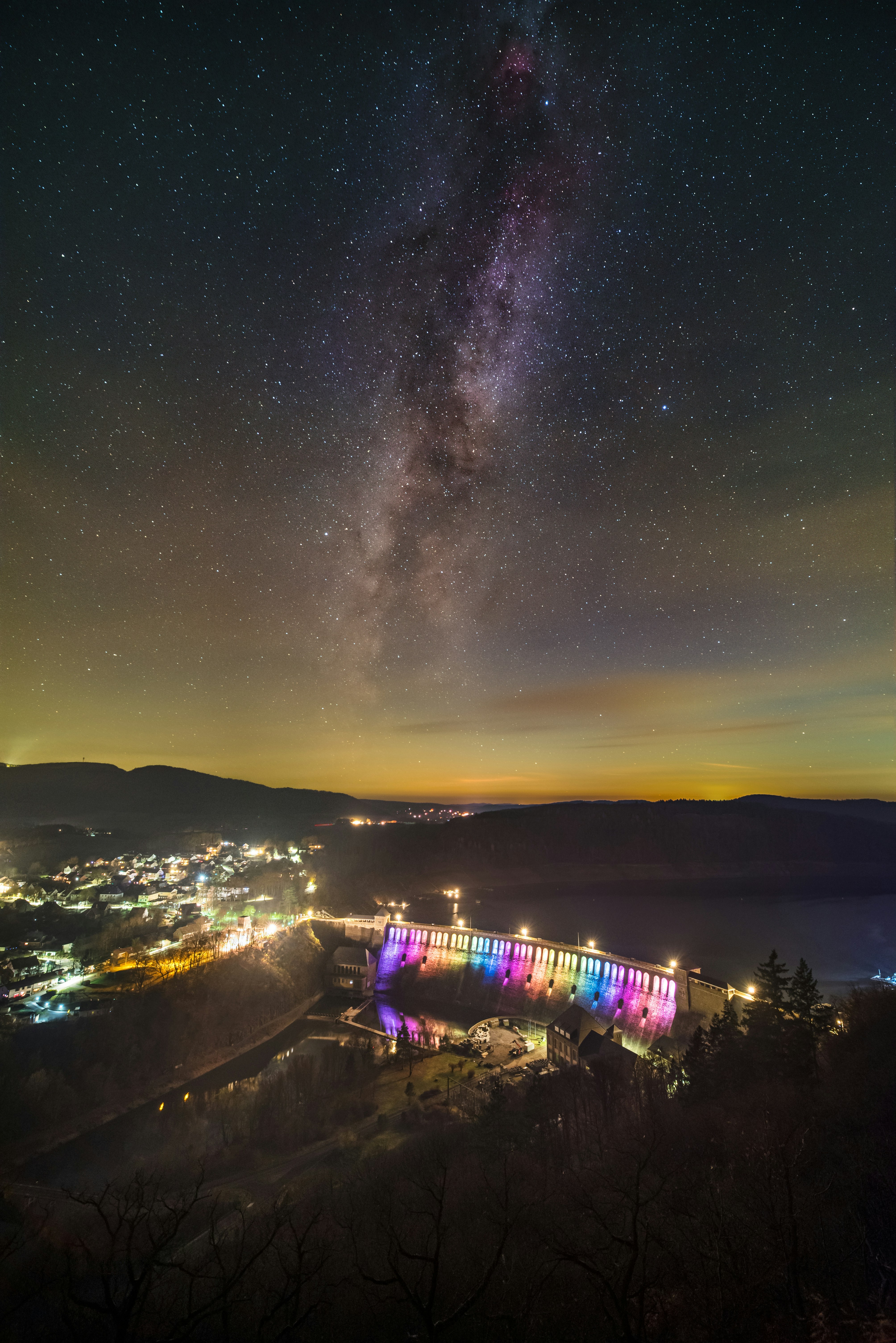 Milky way galaxy over a colorful illuminated dam at night