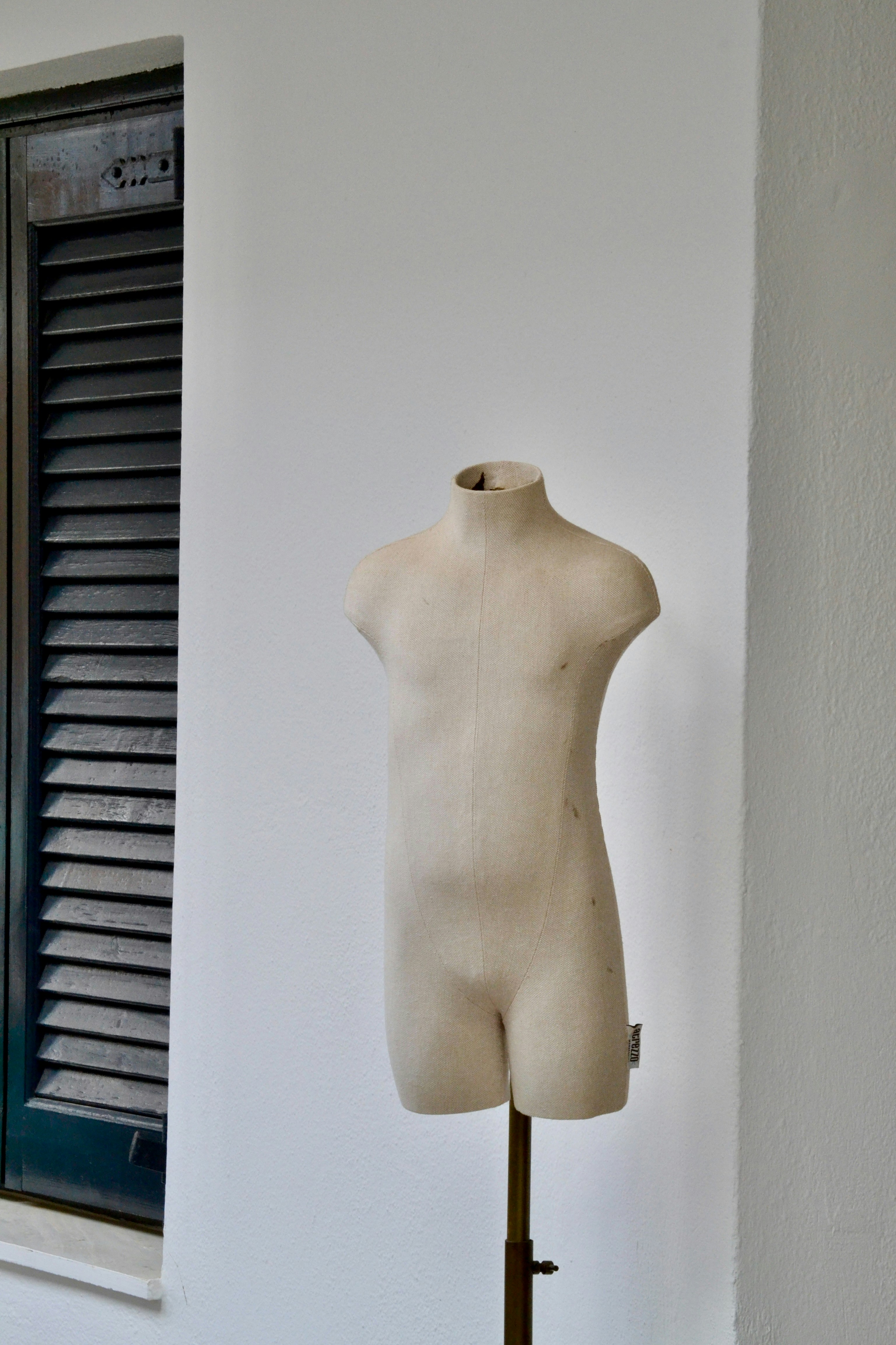 Sebuah manekin tanpa kepala berdiri di dinding putih.