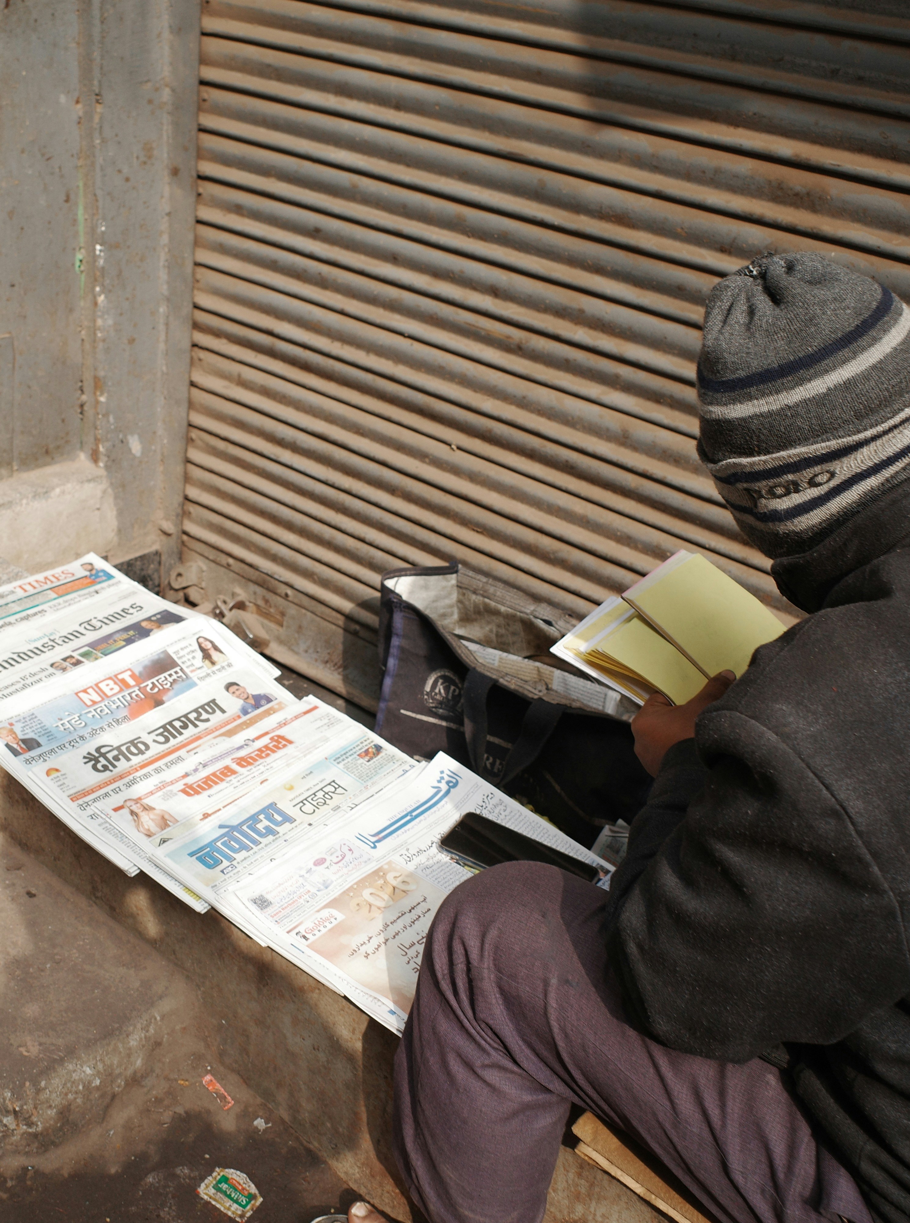 Man in beanie reads near newspapers on sale newspapers