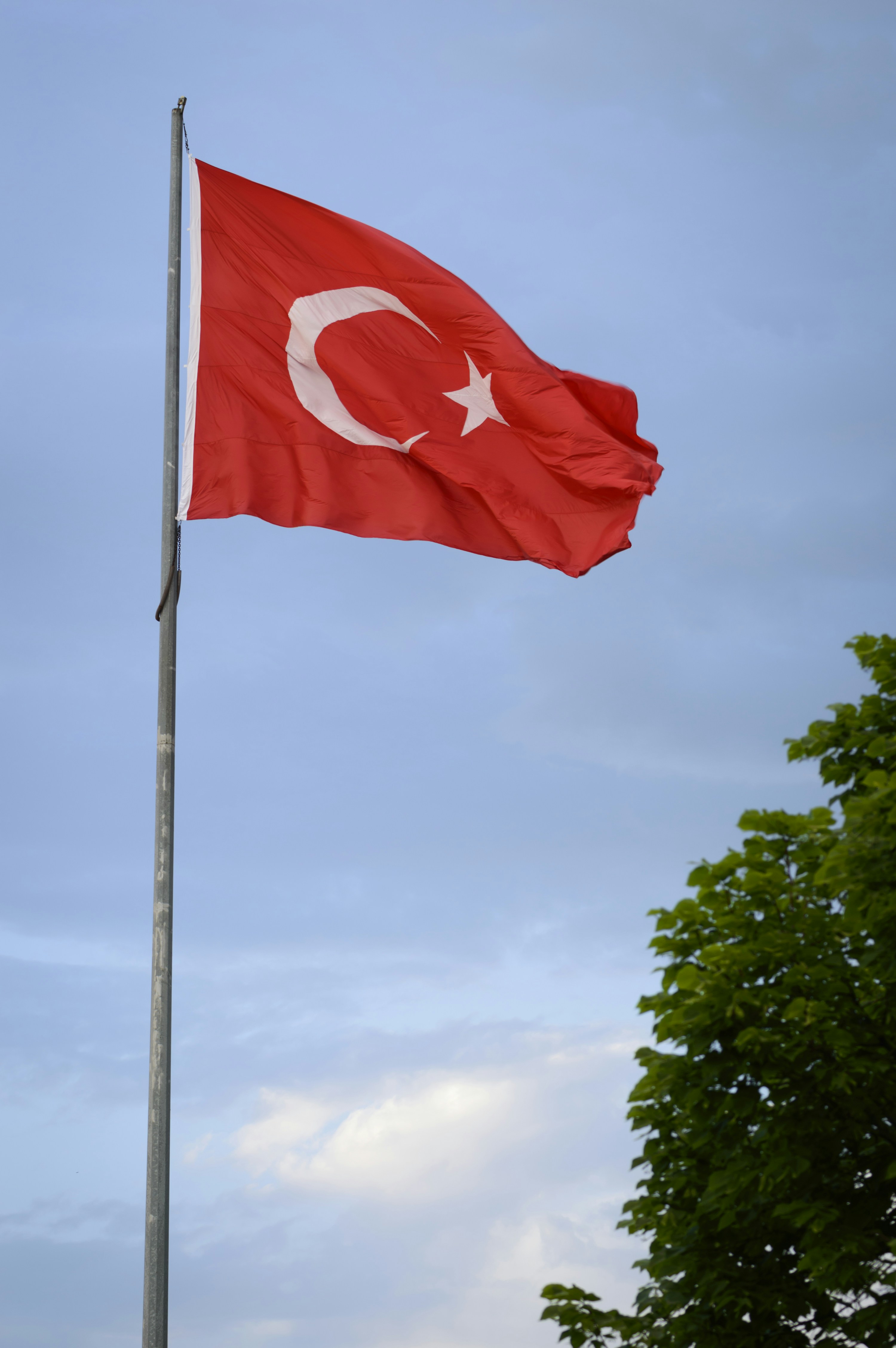 The turkish flag waves against a cloudy sky.