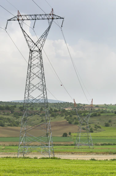 Two tall power line towers in a green field.