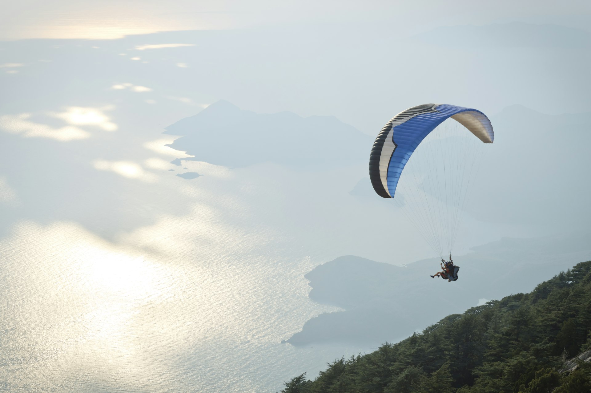 A person paragliding over a scenic coastal landscape.