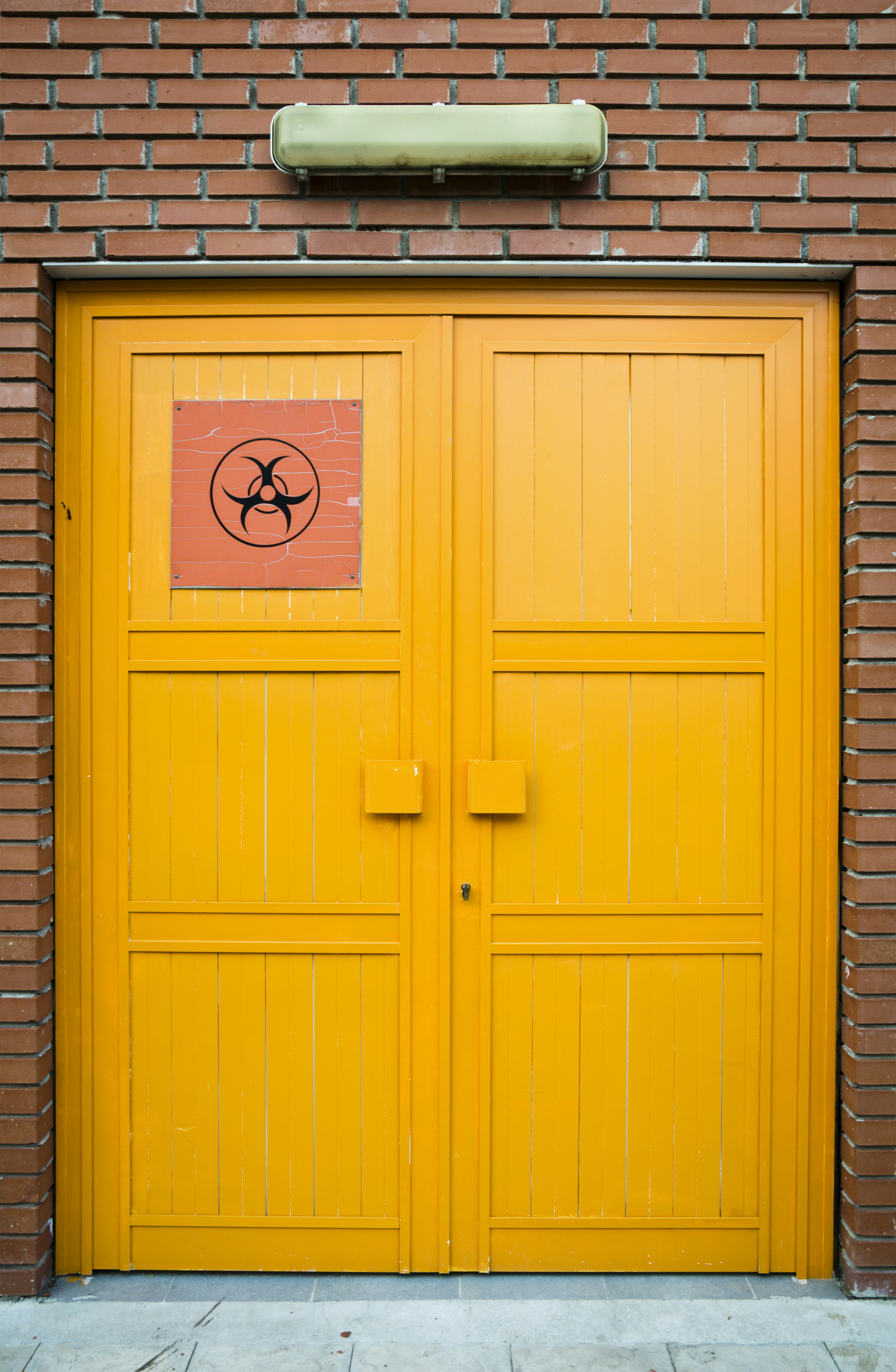 Doppie porte arancioni con il simbolo del biohazard su un muro di mattoni