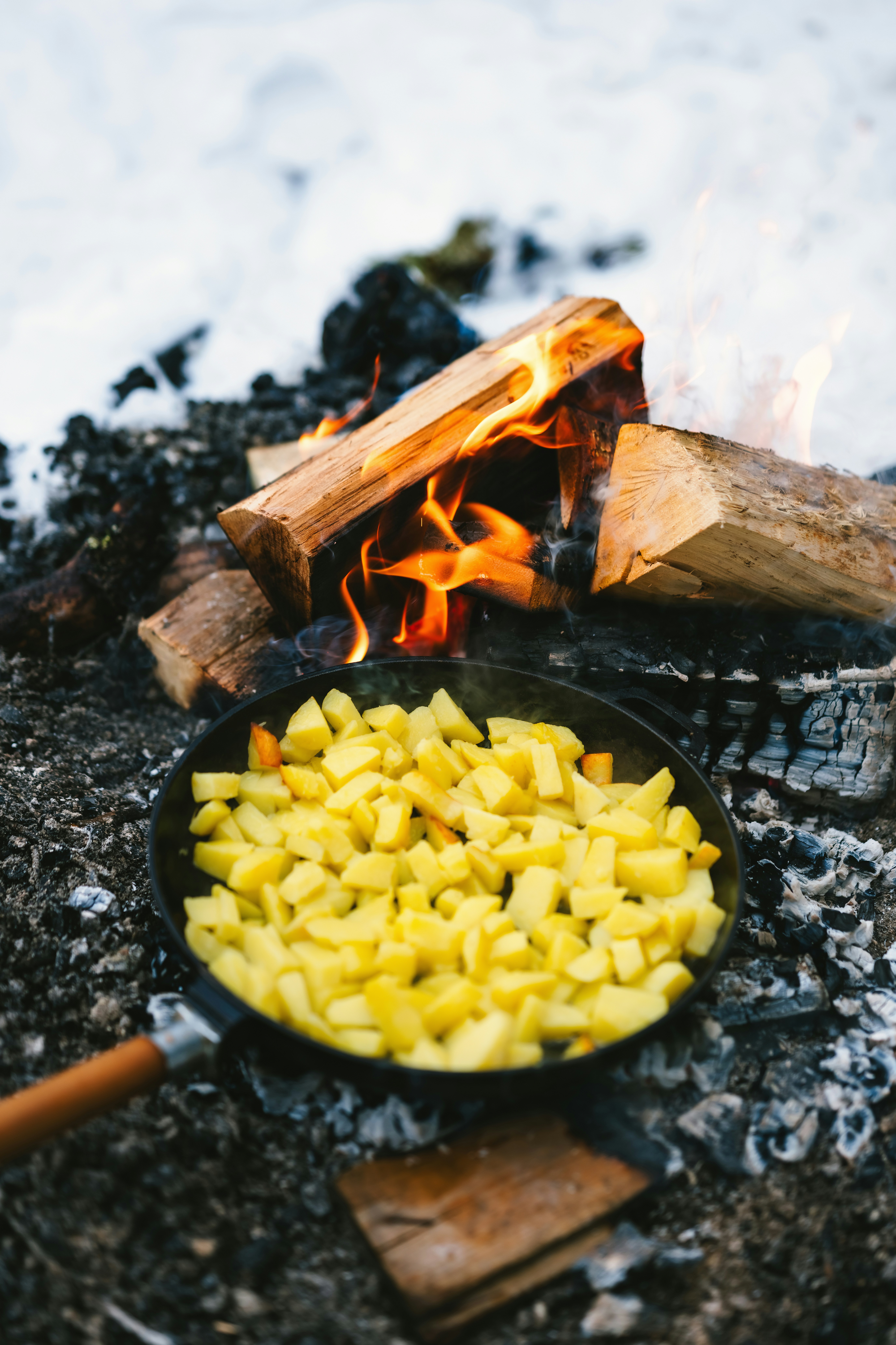 Diced potatoes cooking in a pan over a campfire.