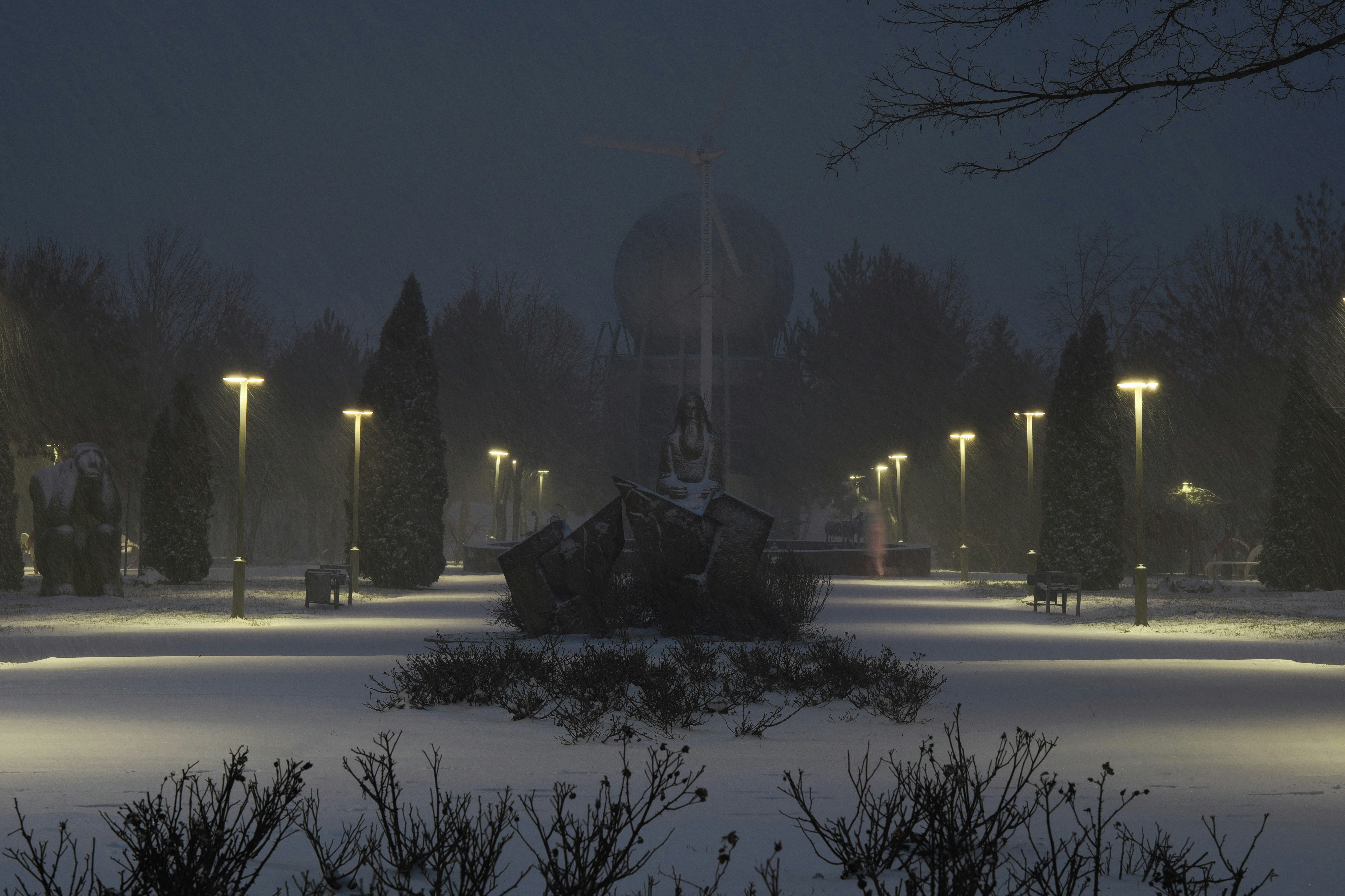 Taman bersalju dengan tiang lampu yang diterangi saat senja