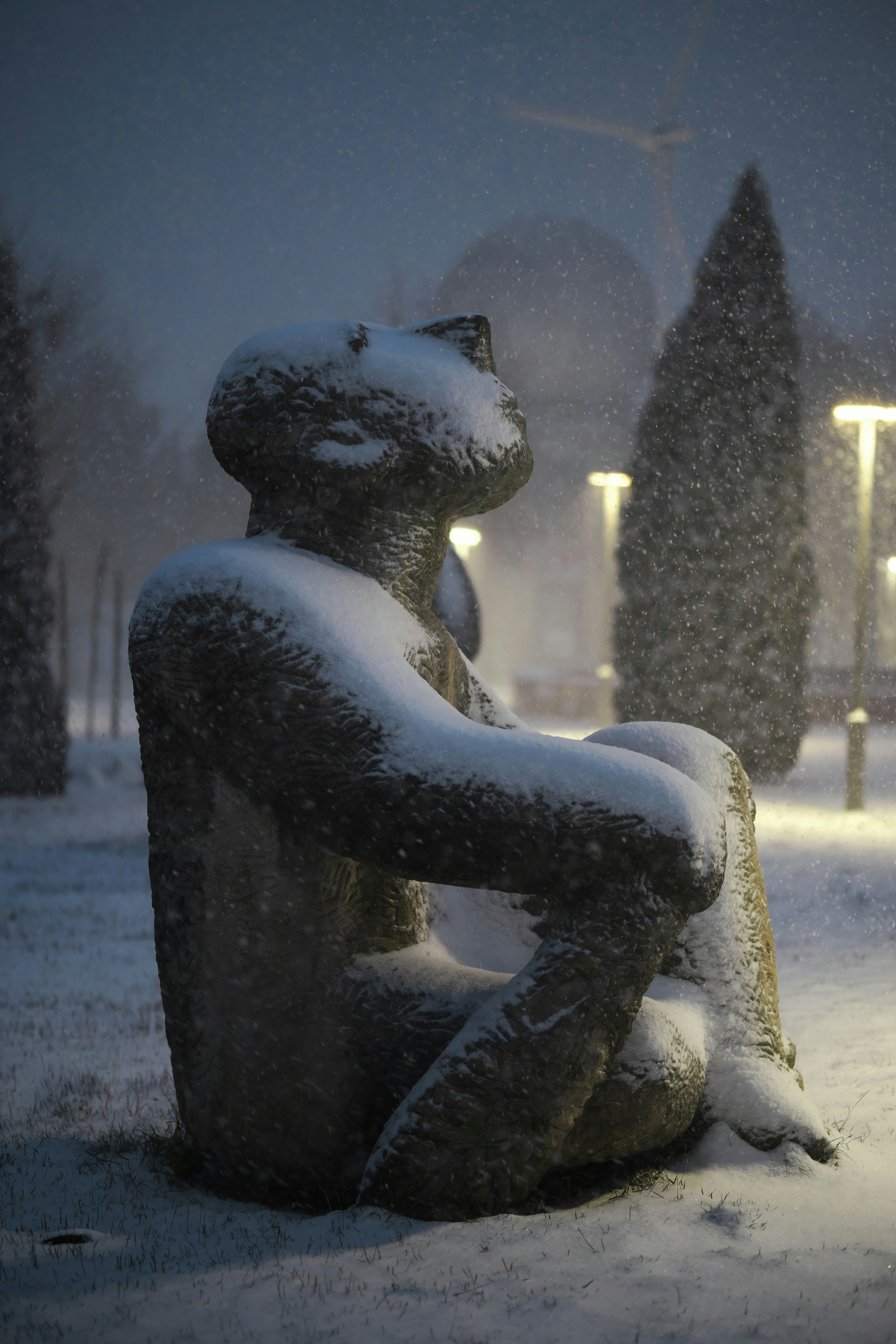 Sebuah patung yang tertutup salju duduk di taman pada malam hari.