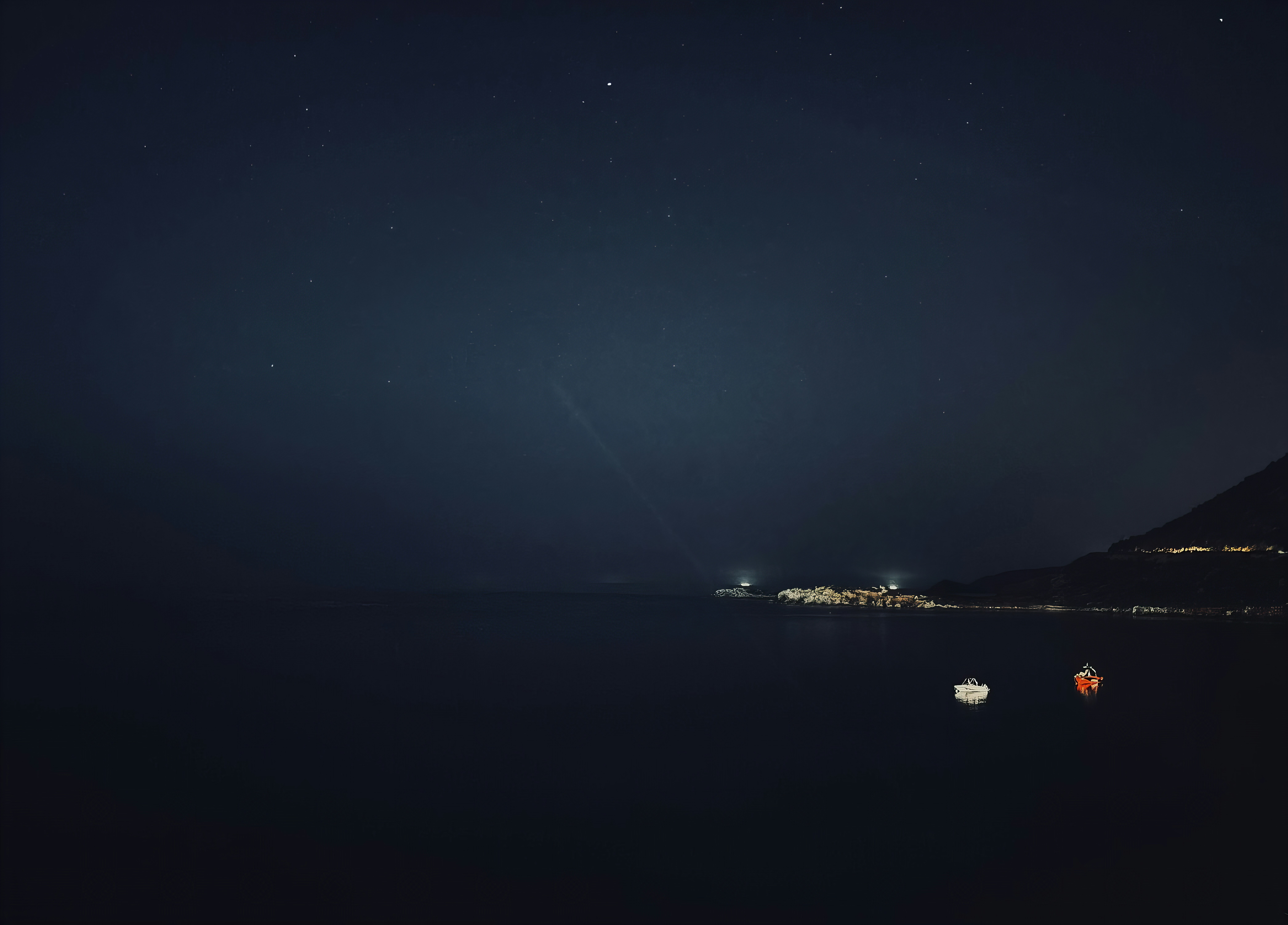 夜の暗い海に遠くの灯りがきらめいている。