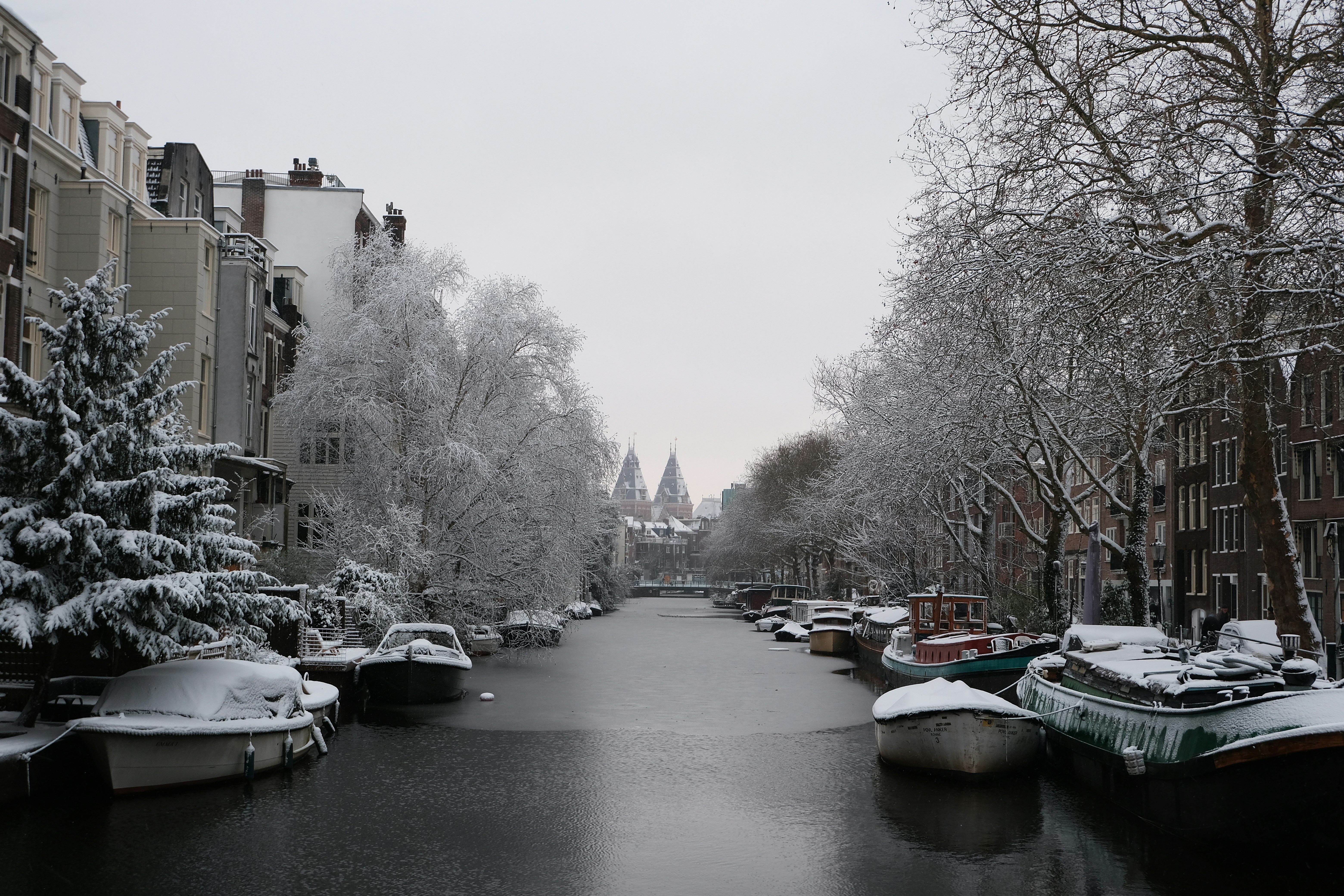 Canal nevado con barcos y árboles desnudos en Ámsterdam.