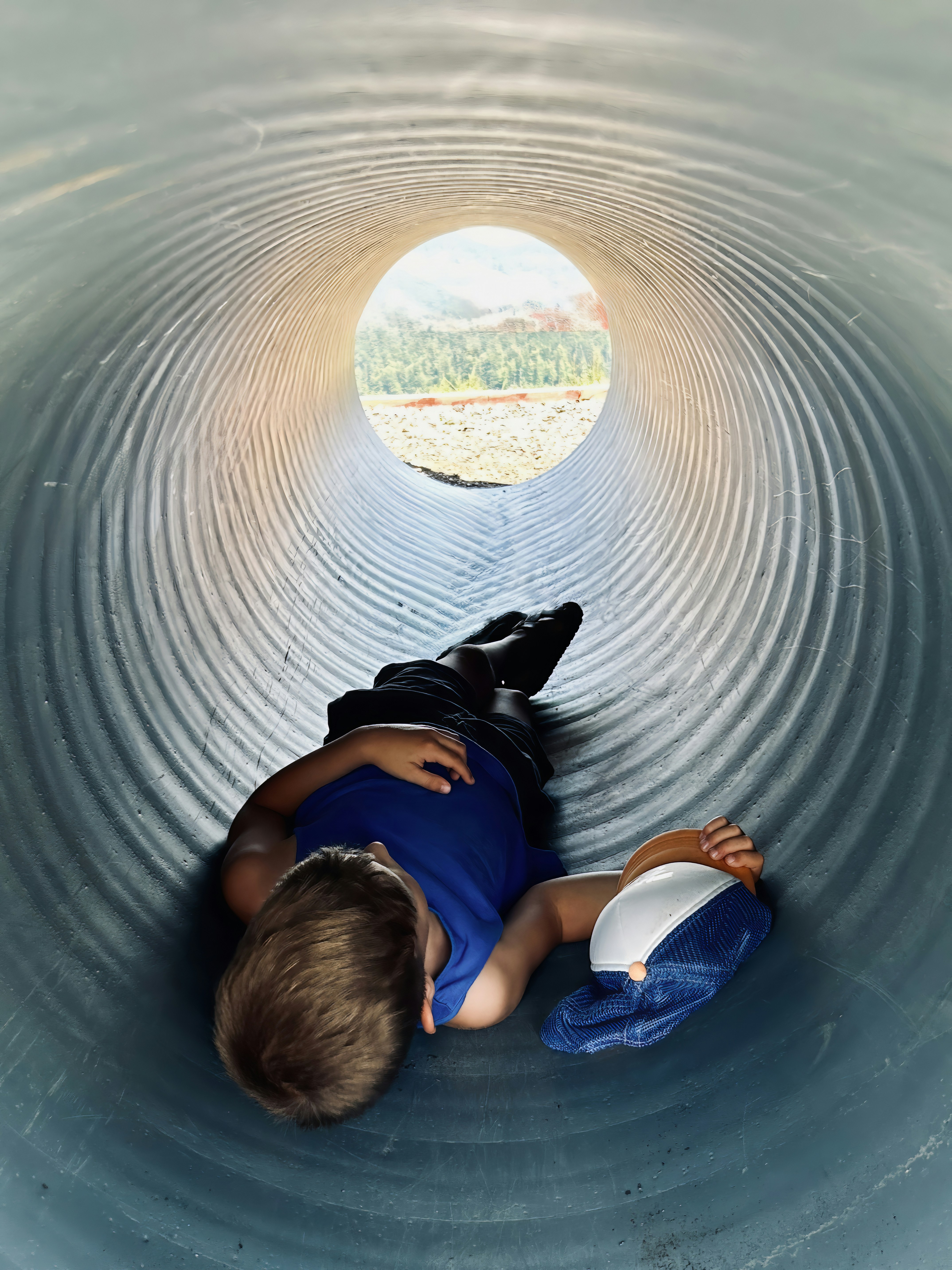 大きな金属パイプの中に横たわる少年が外を見ている。