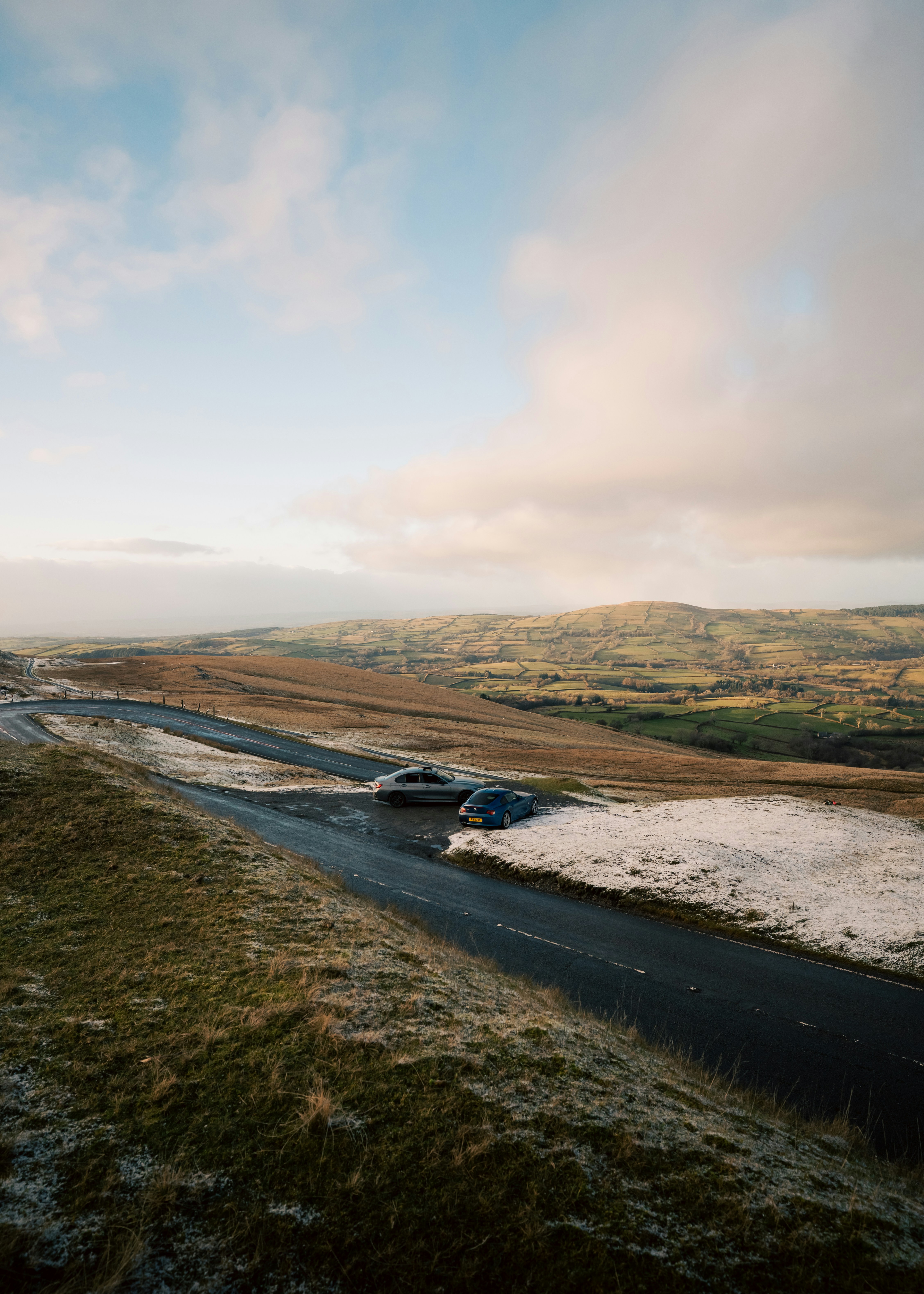 Two cars on a winding road in a hilly landscape.