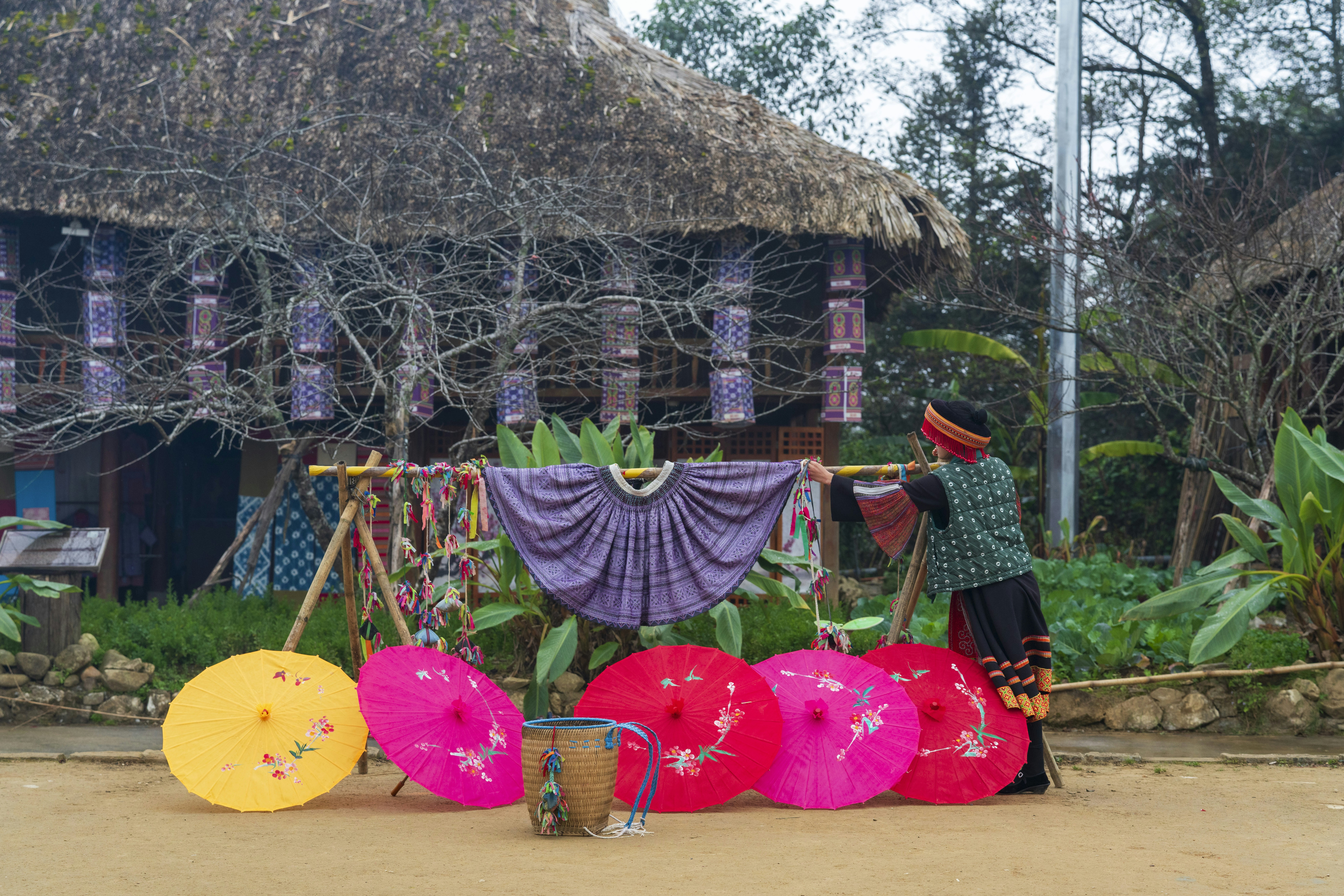 Person arranging colorful umbrellas outside traditional hut