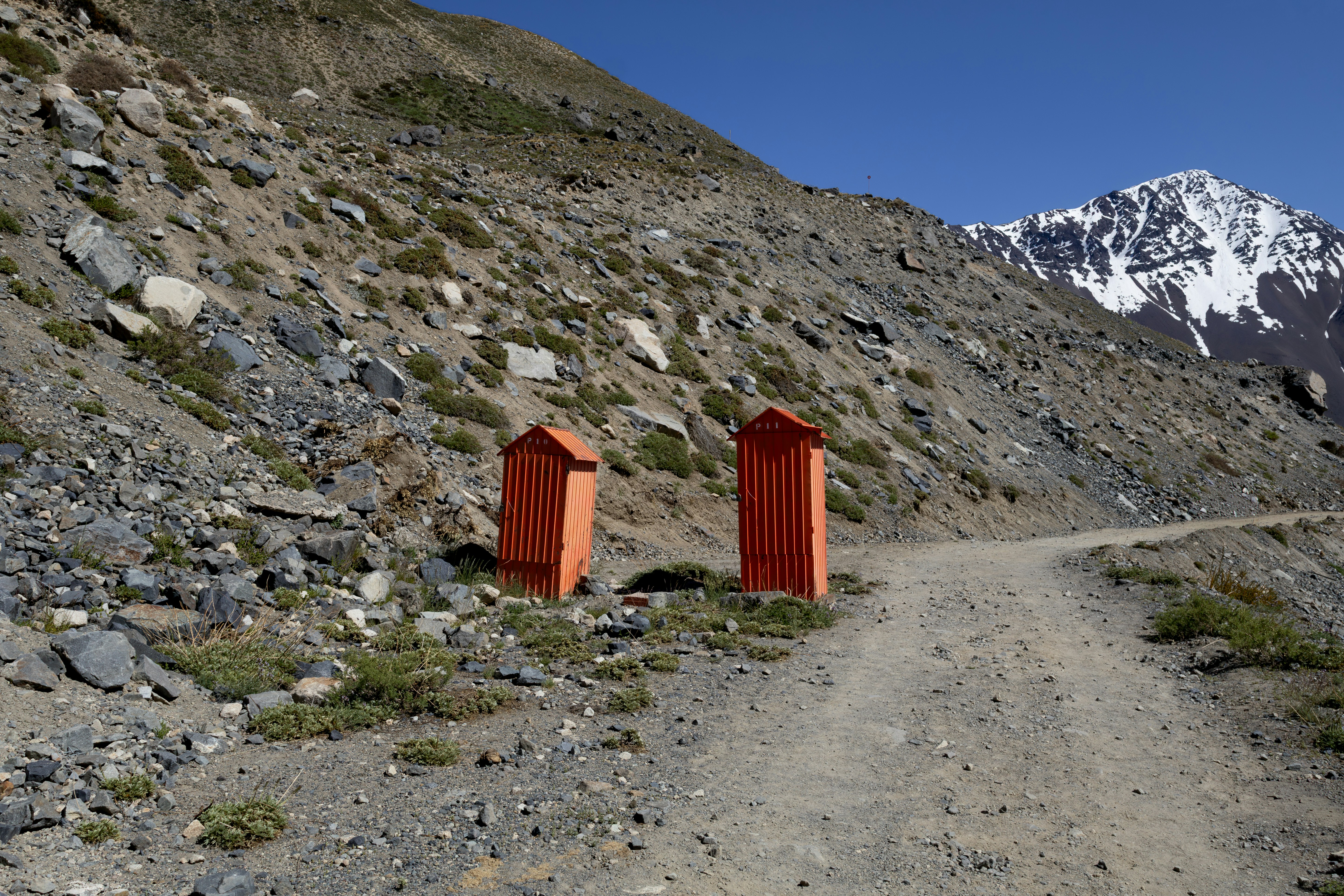 Two orange outhouses on a dirt road in mountains