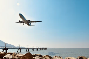 Airplane landing over the ocean near a pier.