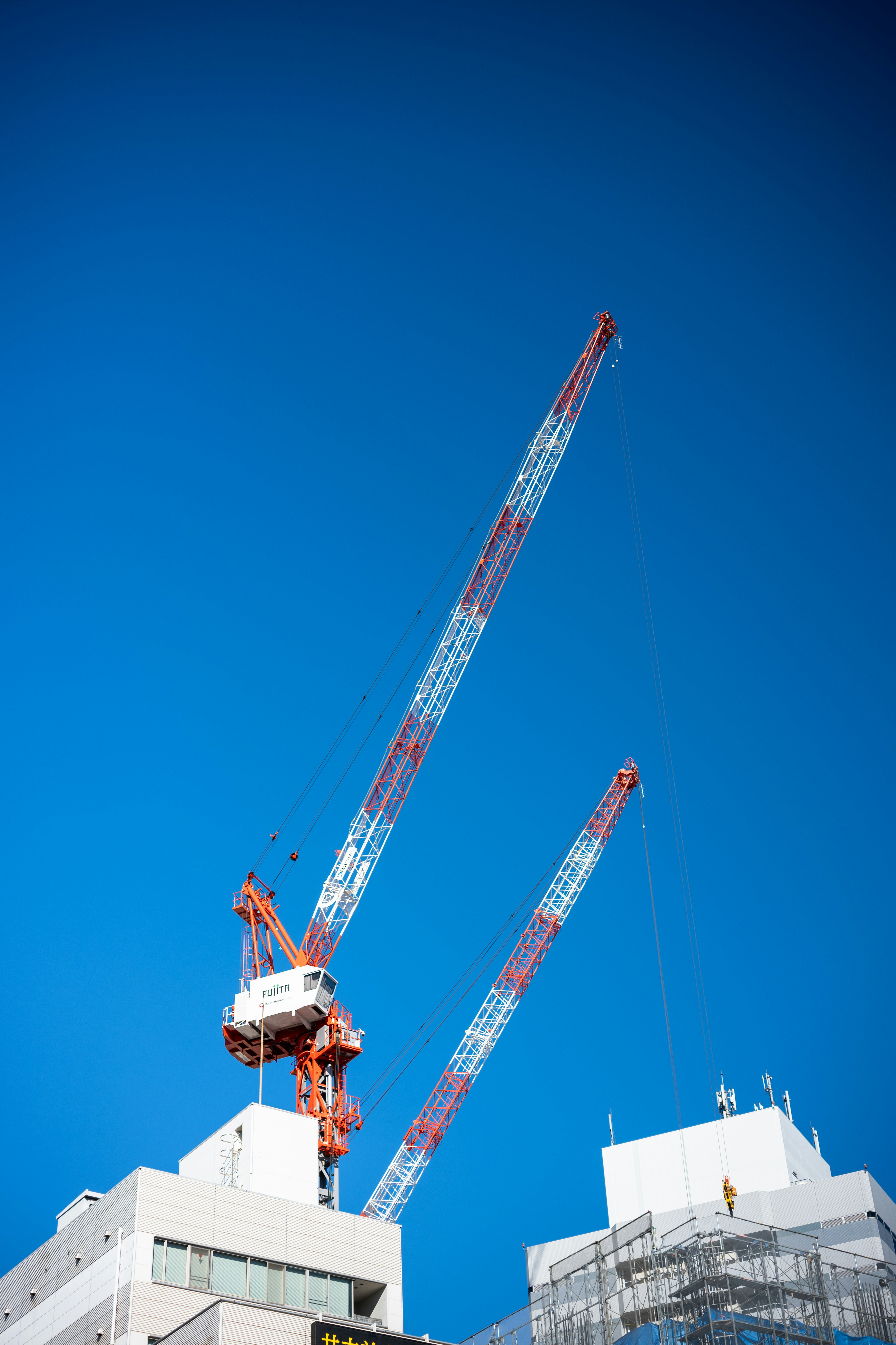 Two construction cranes against a clear blue sky.