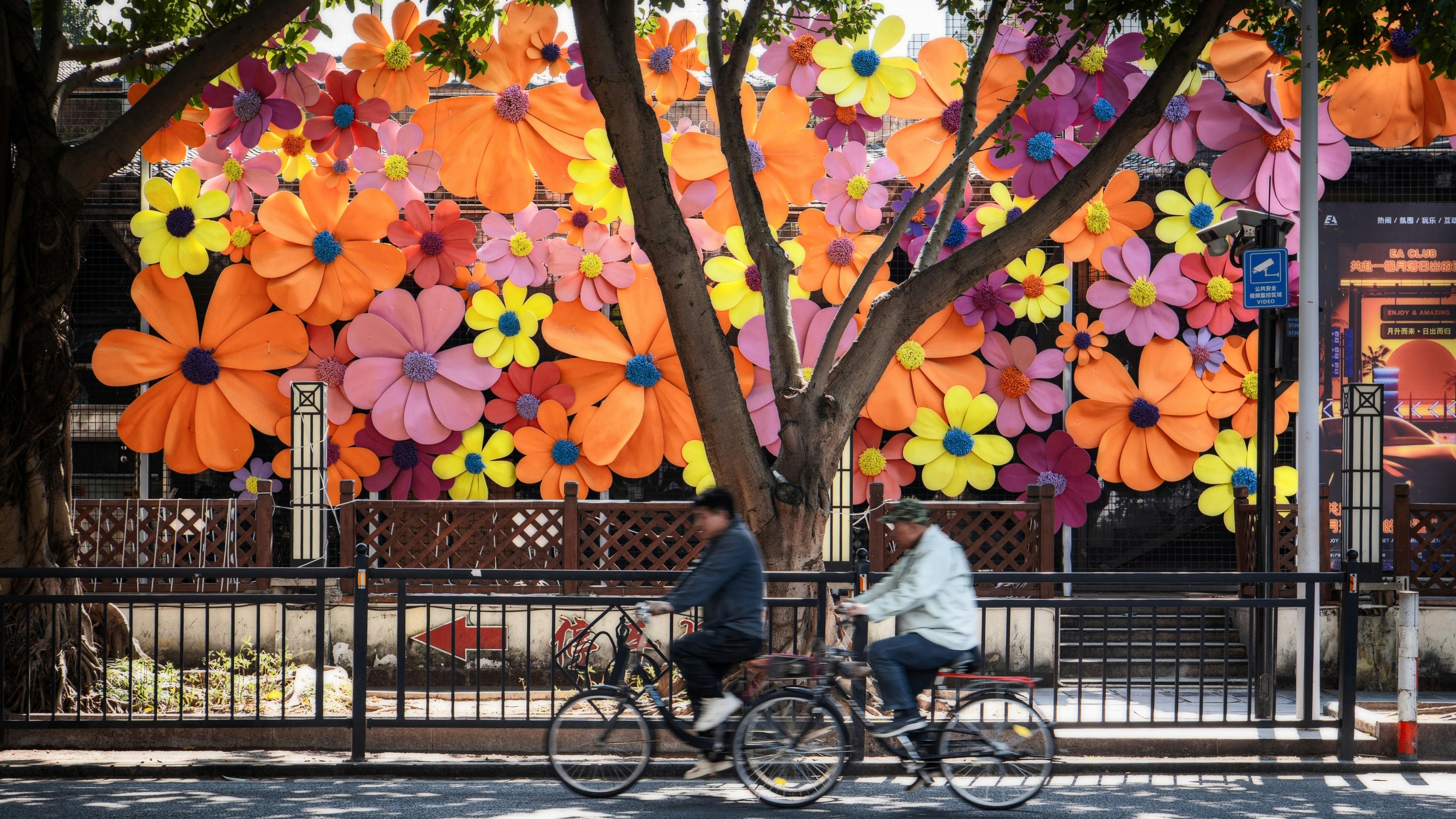 Two people cycling past a vibrant floral mural.