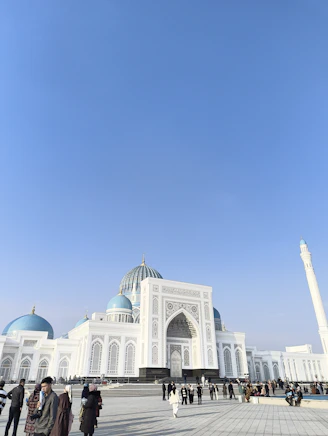 A white mosque with blue domes under a clear sky