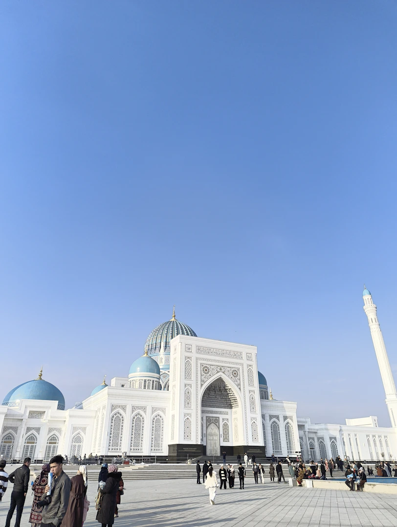 A white mosque with blue domes under a clear sky