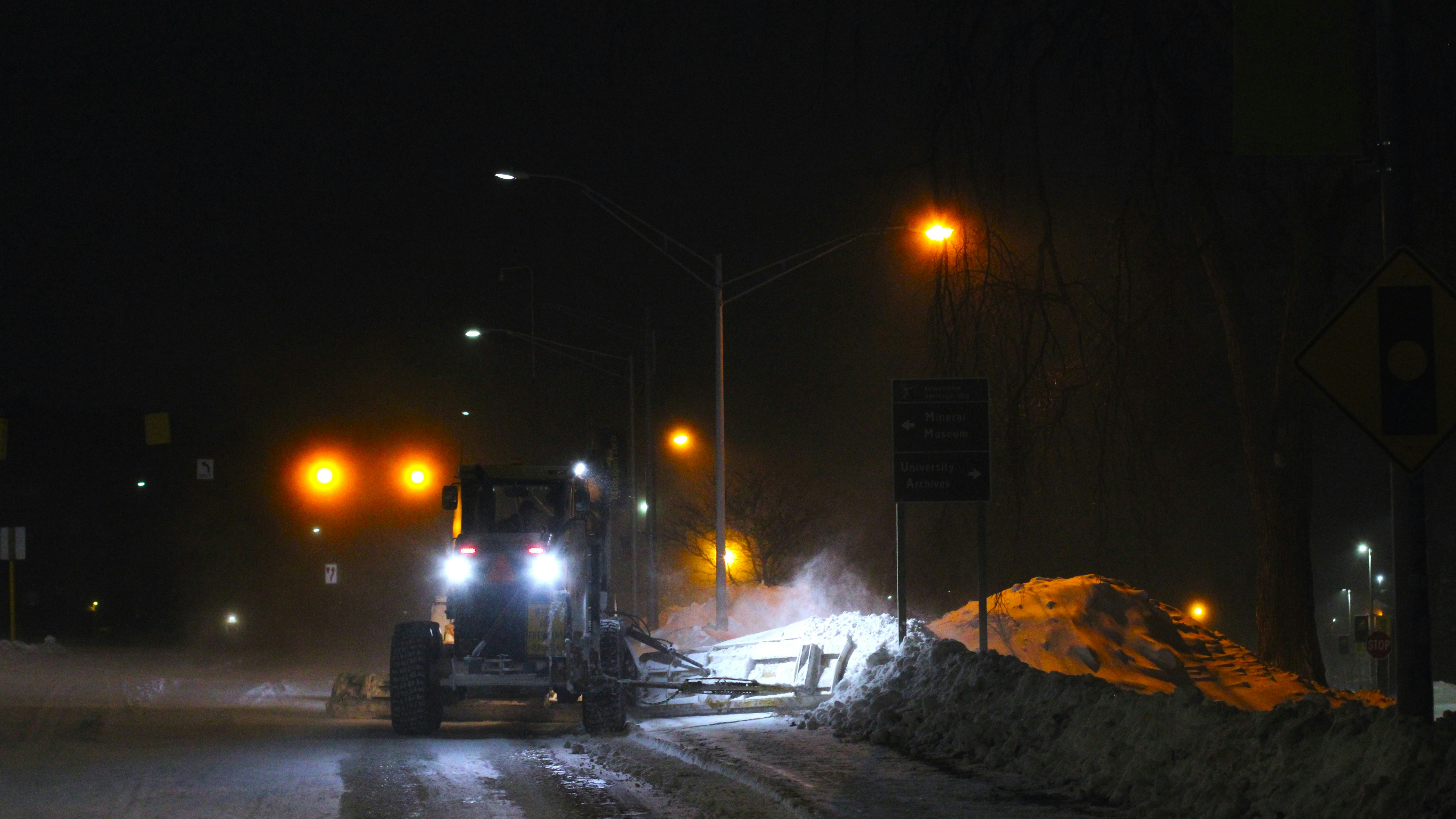 Tractor plowing snow on a street at night.
