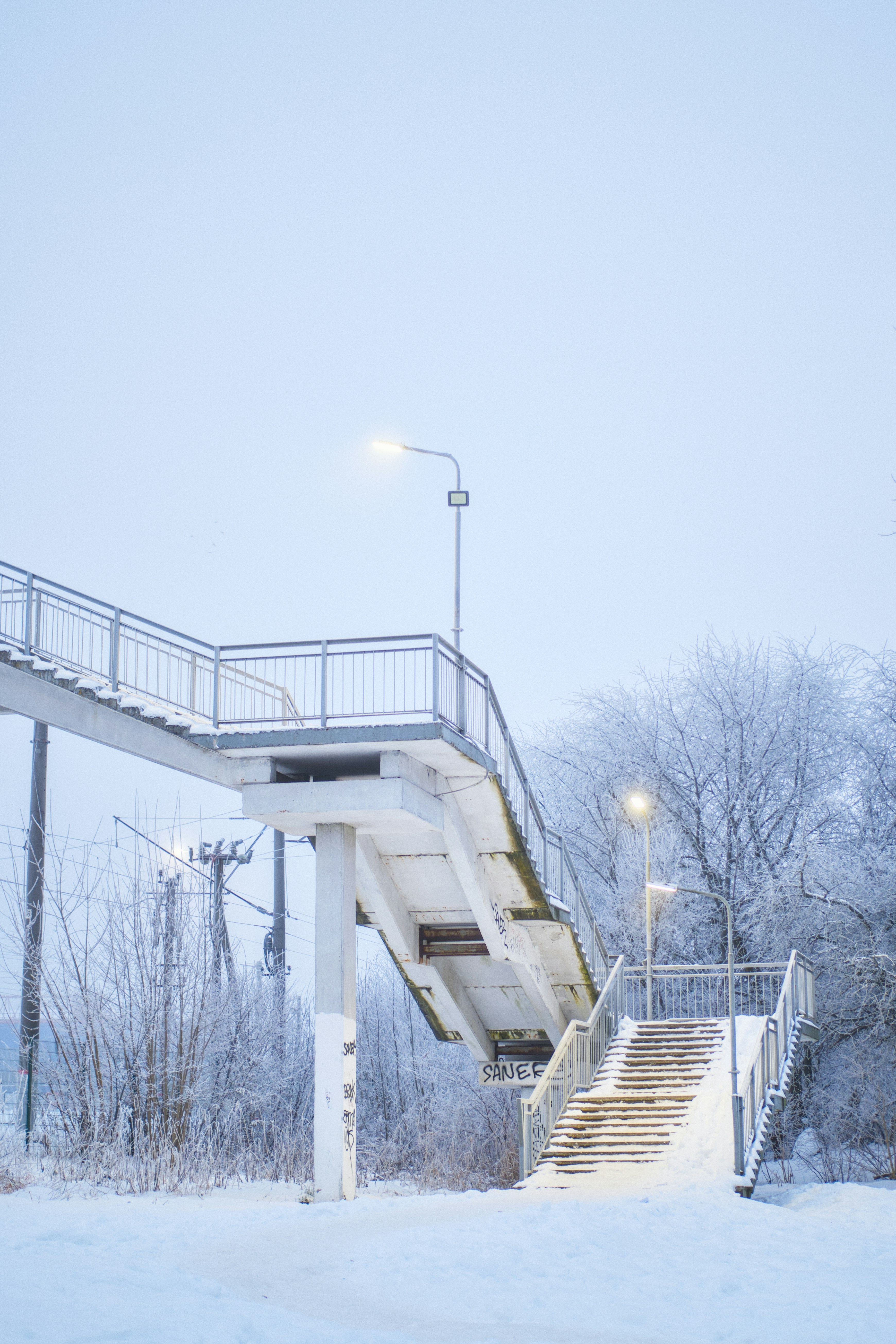 Snowy pedestrian overpass with lights at dusk