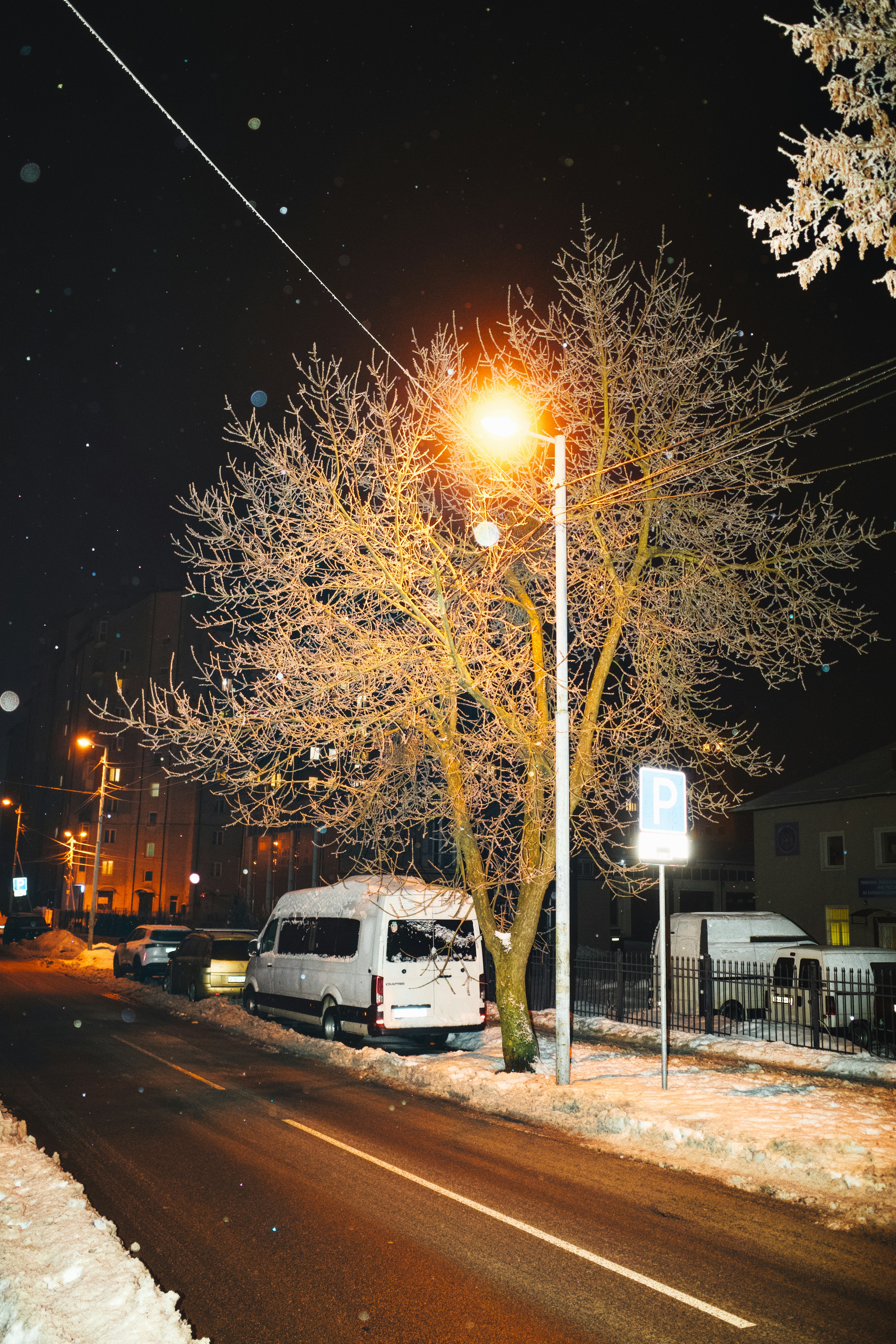 Snowing at night with a street light and van.