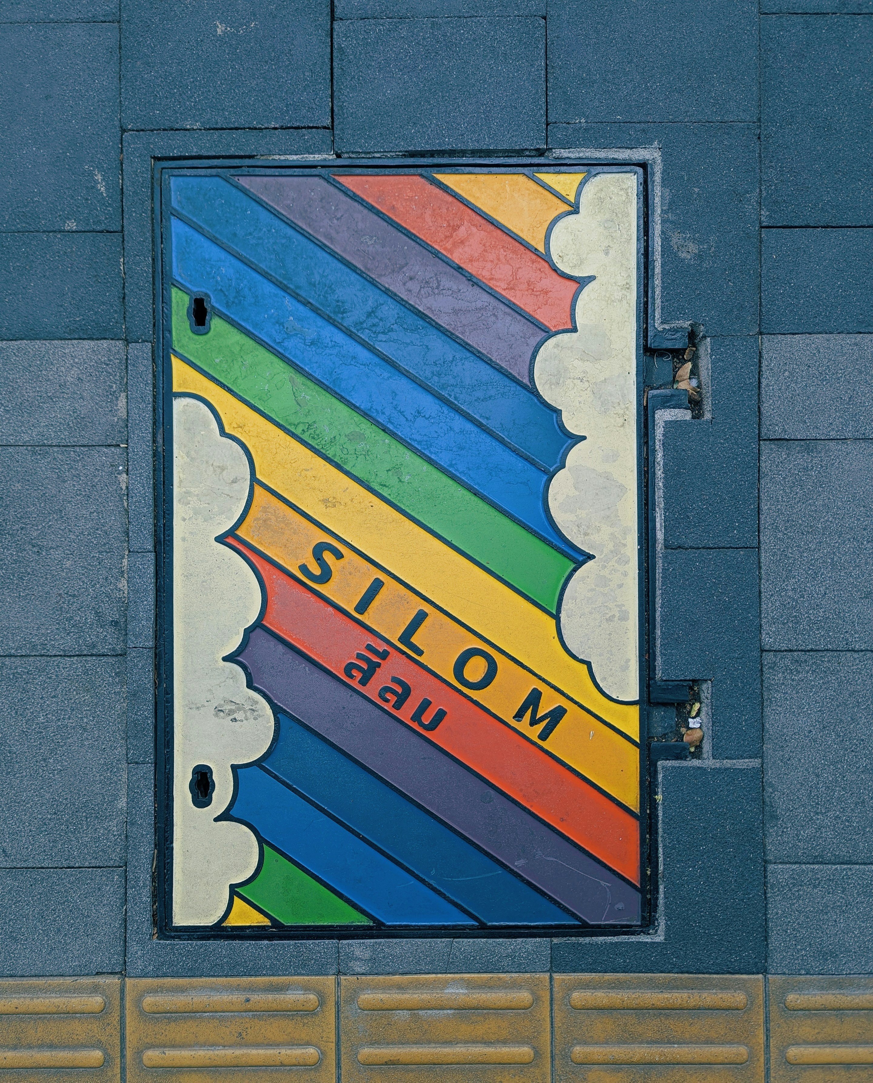 Colorful rainbow manhole cover with "silom" text.