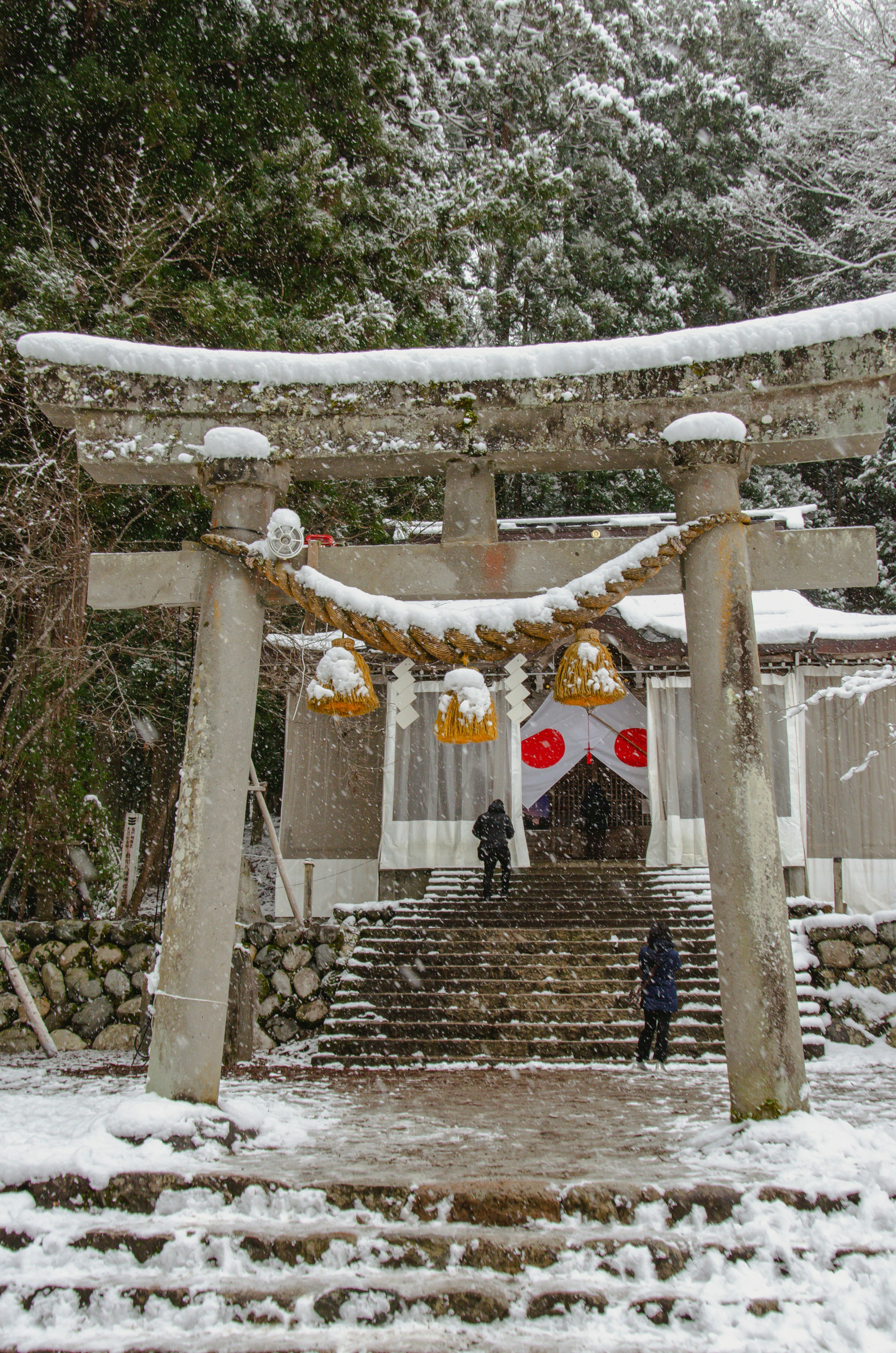 Snowy torii gate leading to a shrine with two people.