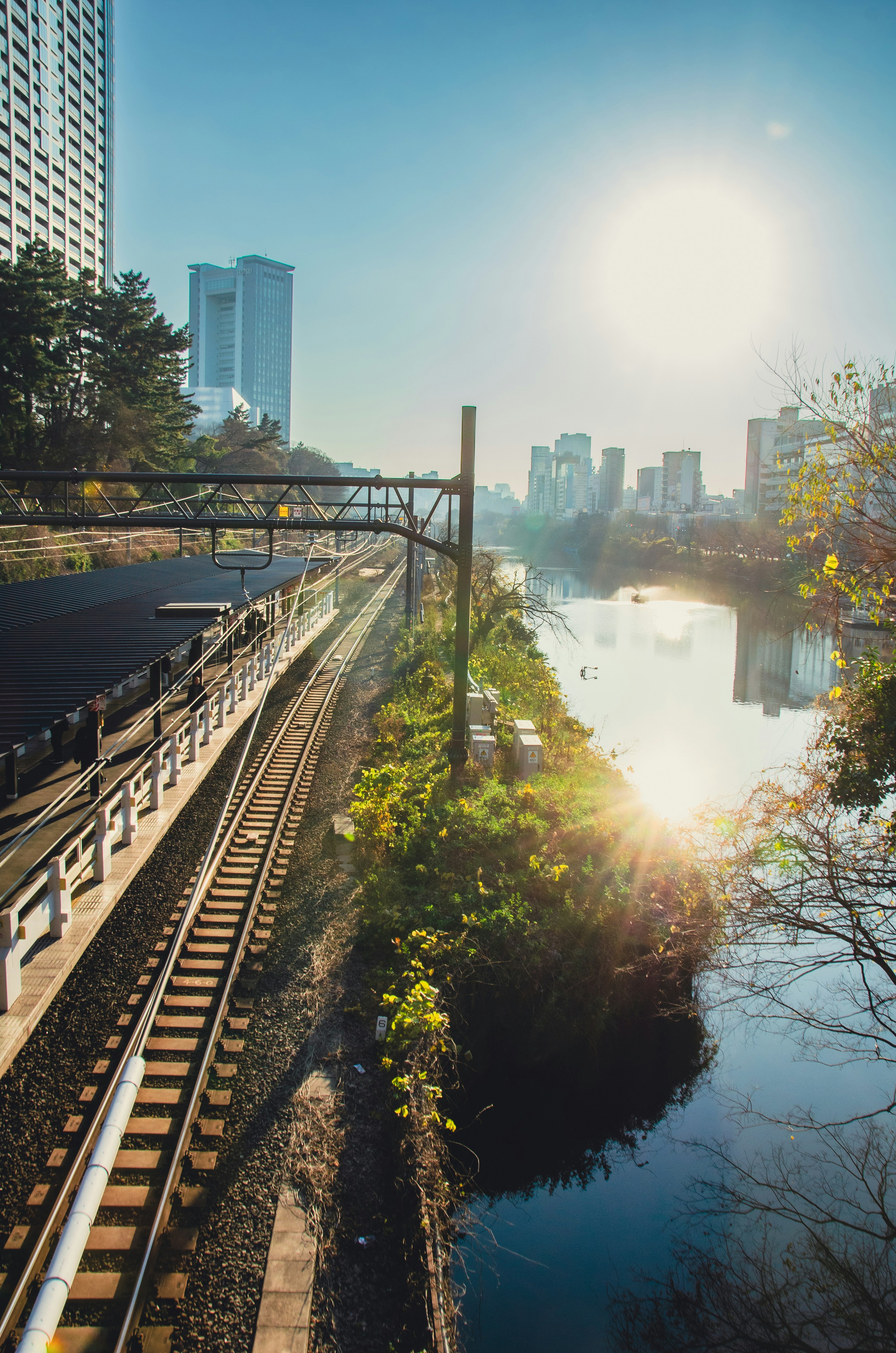 Sunny cityscape with train tracks and river reflection.