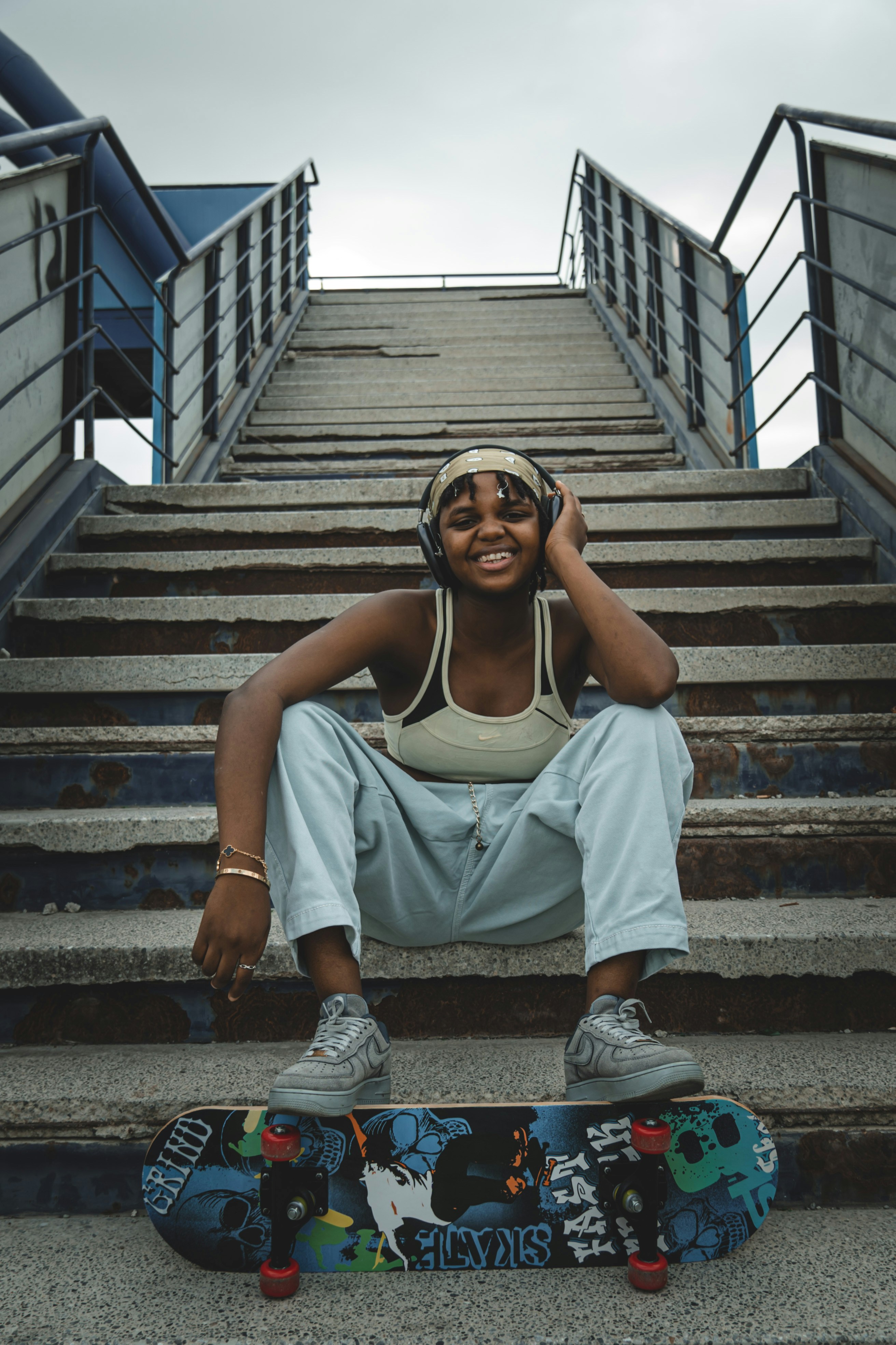 Jeune femme avec un casque assise dans les escaliers avec un skateboard.
