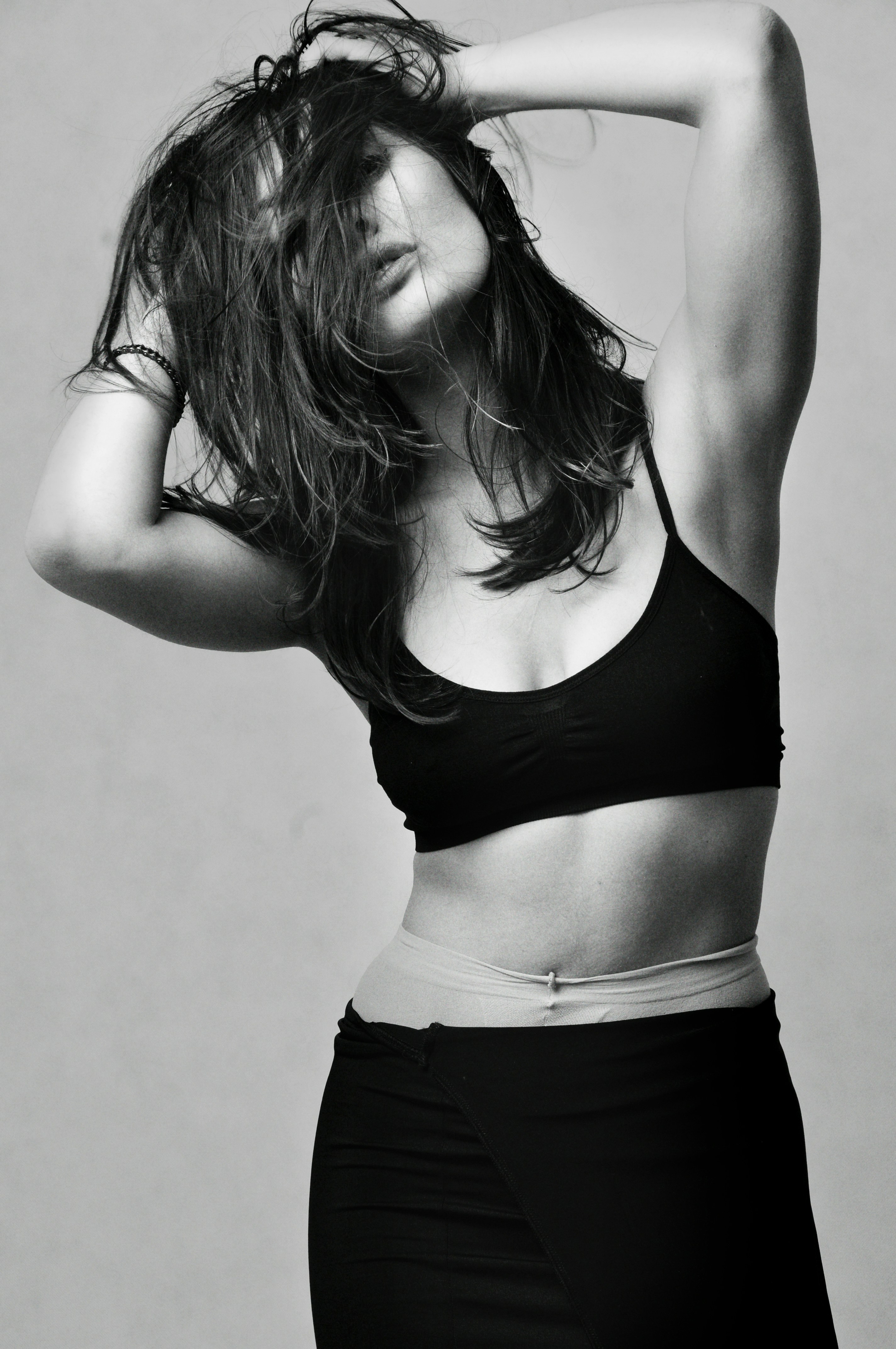 Frau mit den Händen in zerzausten Haaren, trägt schwarzes Oberteil.