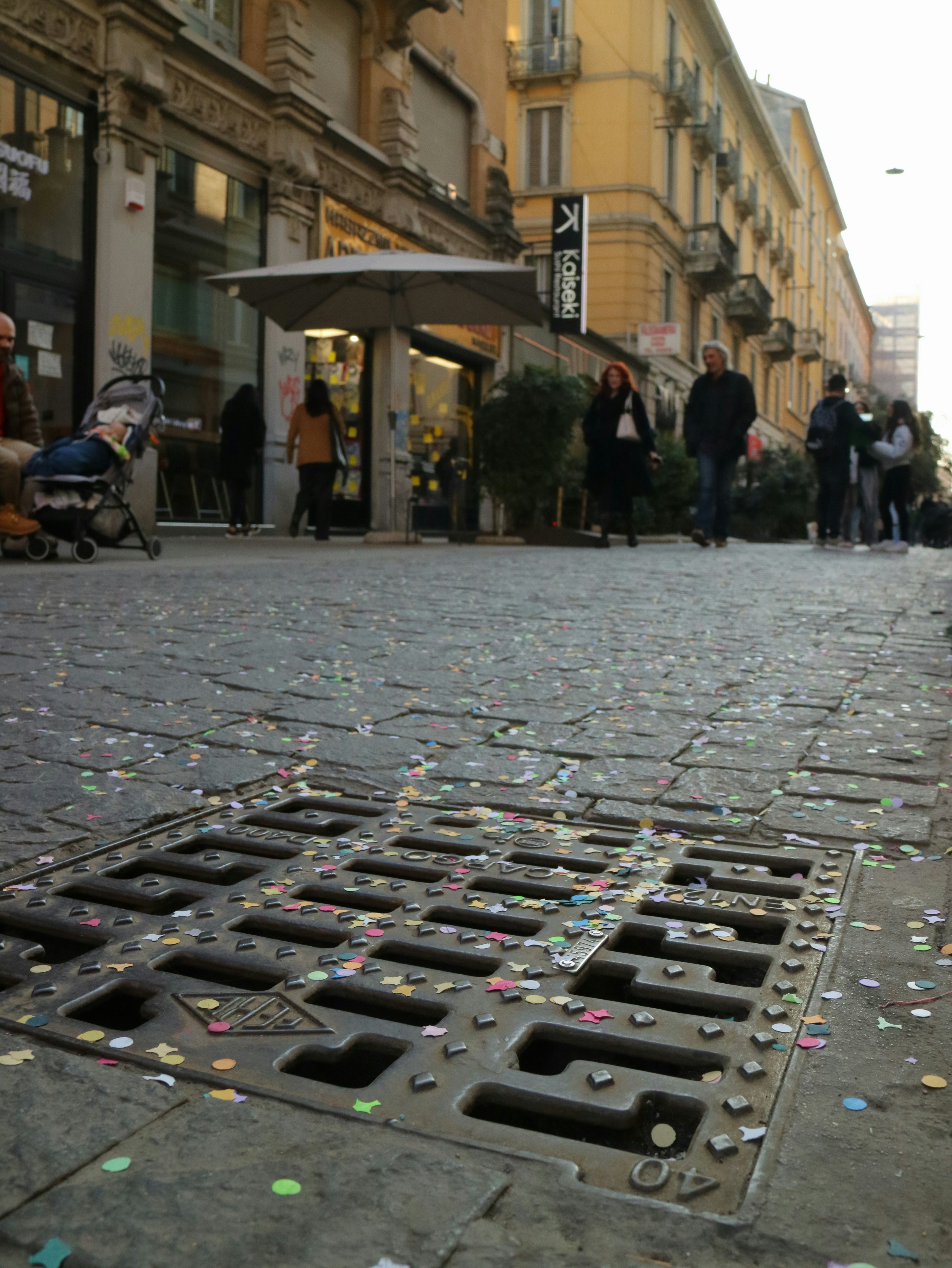 Confetti scattered on a cobblestone street with people walking.