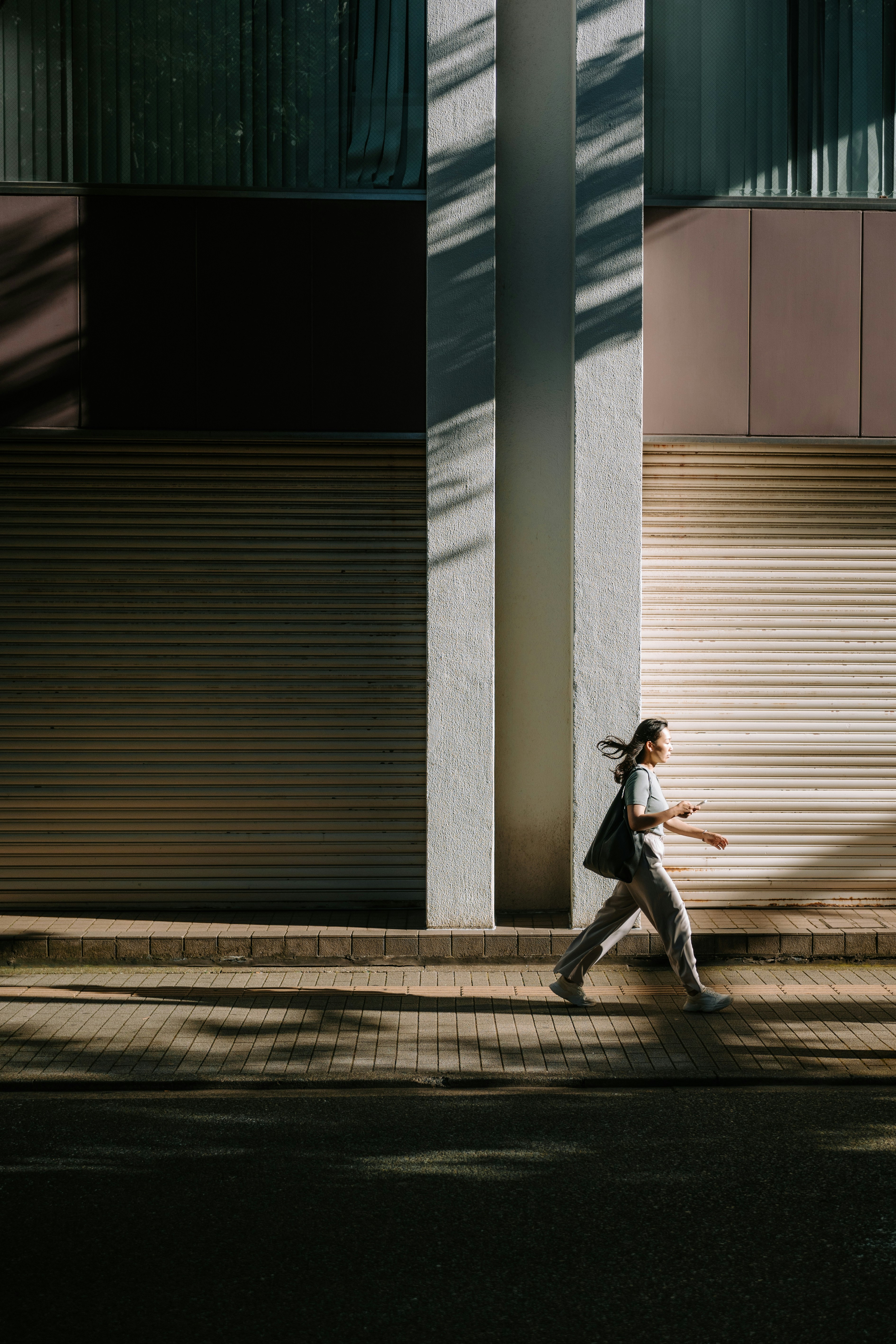 Woman walking on sidewalk with building shadows