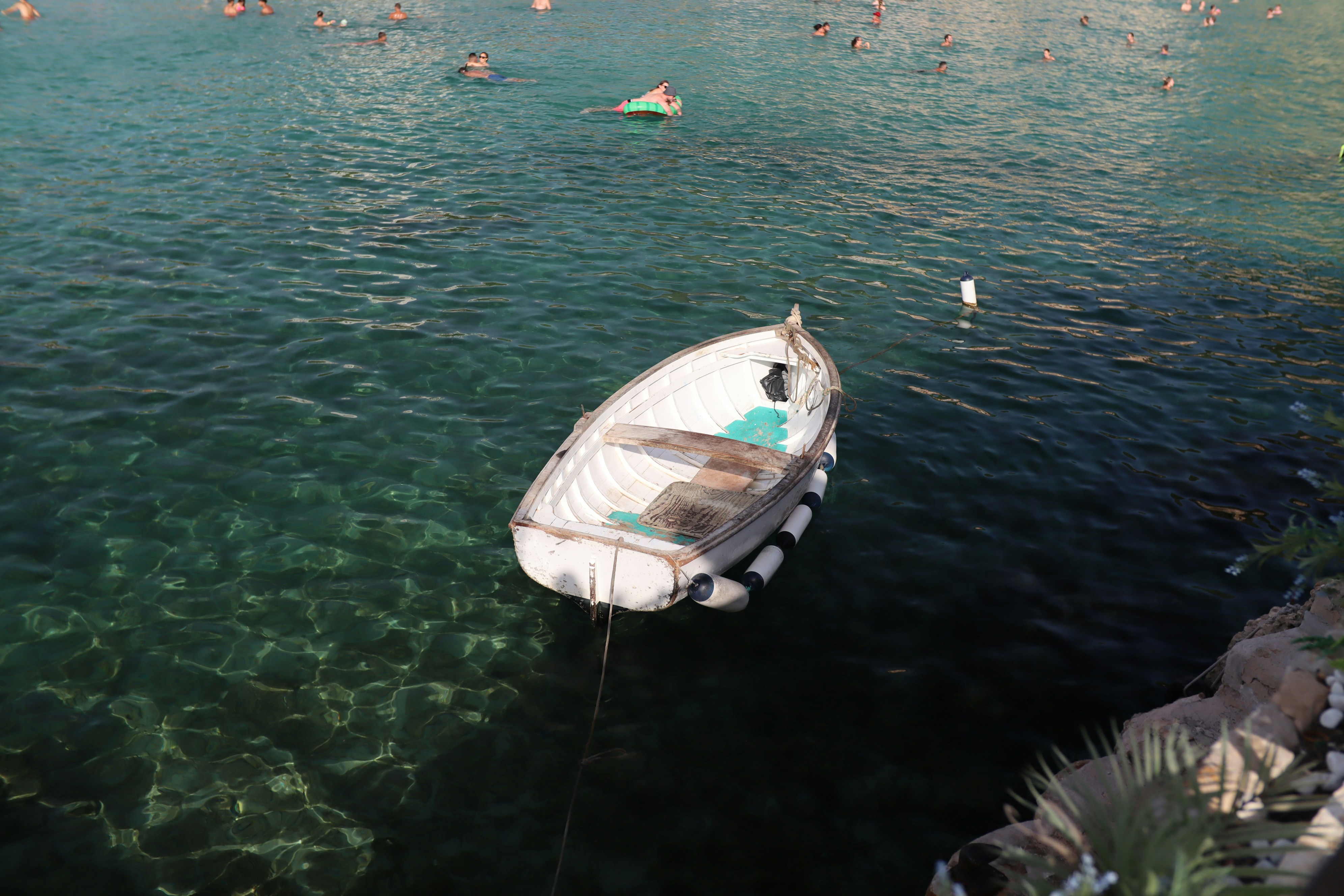 A small boat floats on clear turquoise water near shore.