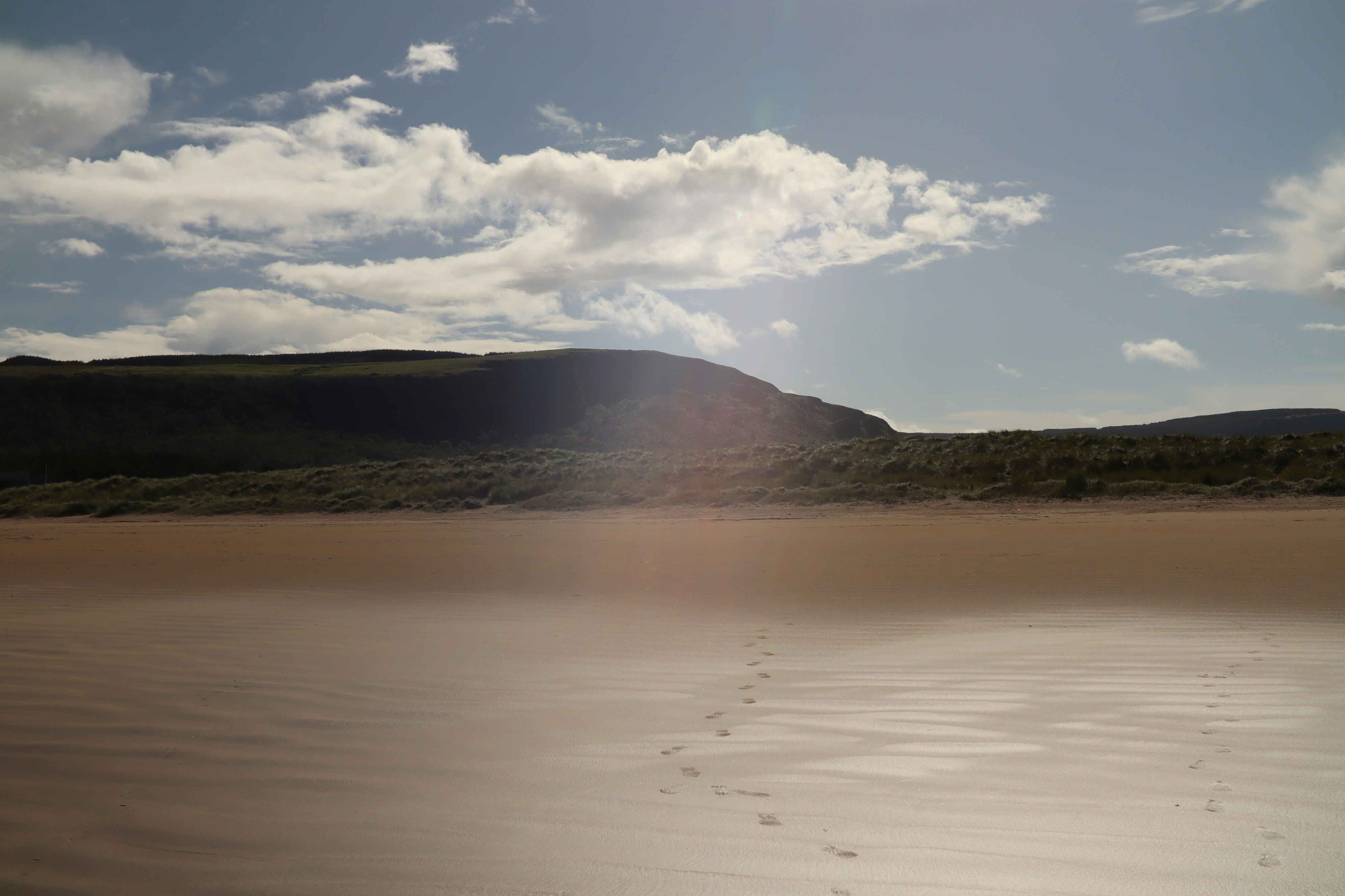 Footprints on a sandy beach with distant hills