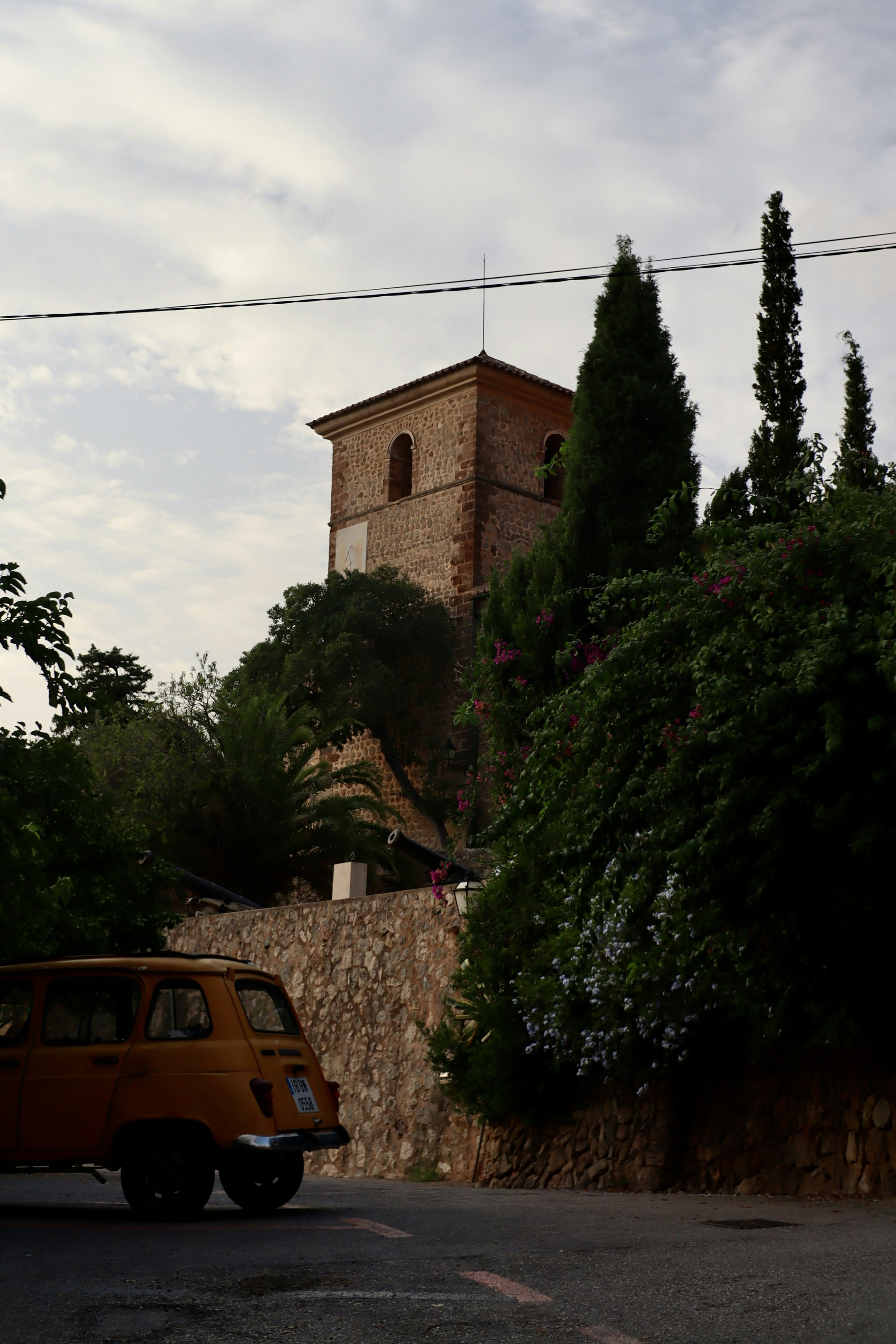 Old brick tower overlooks lush green trees and yellow car.