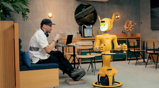 Man in cafe interacts with a yellow robot.
