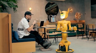 Man in cafe interacts with a yellow robot.