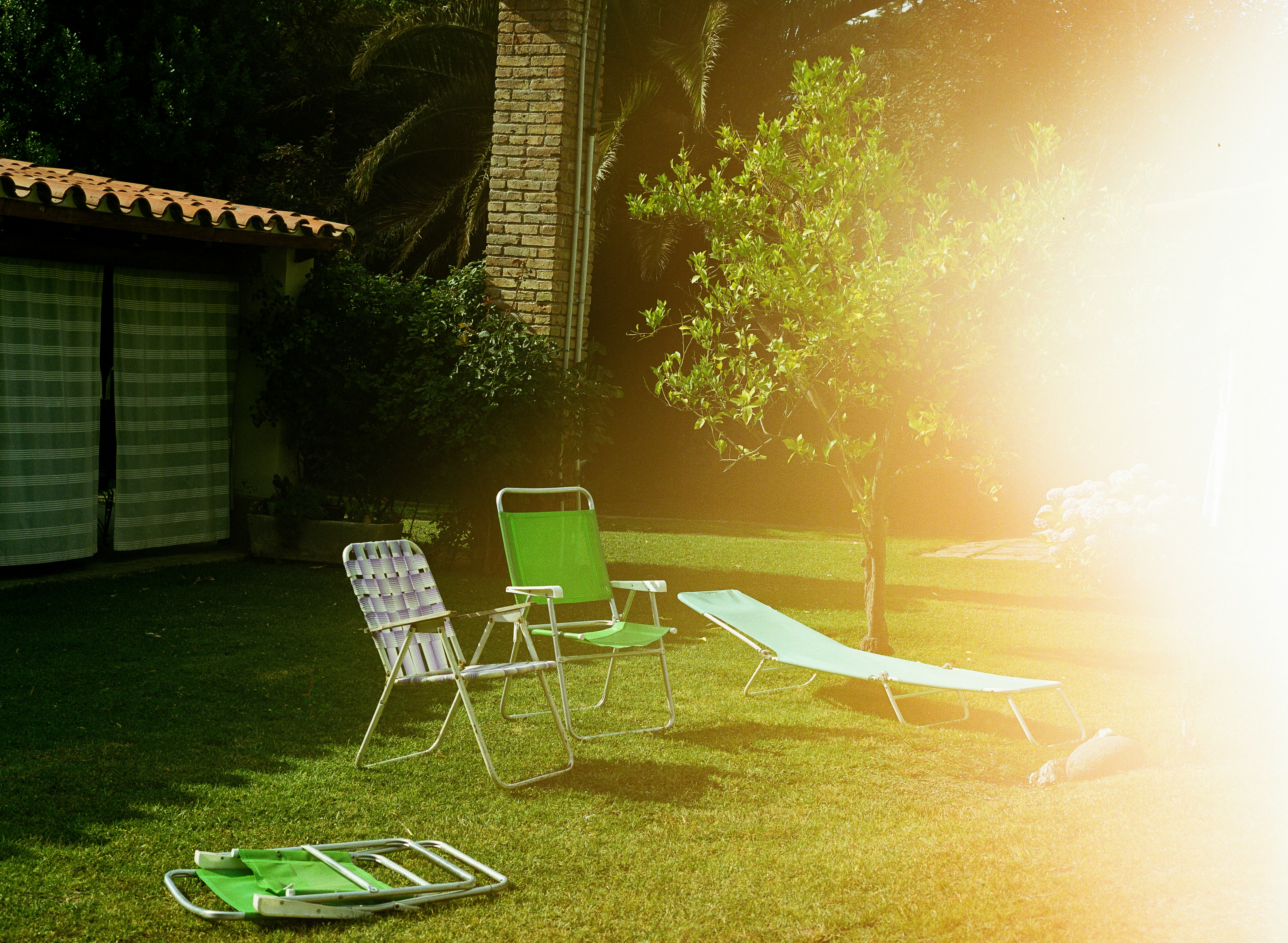 Lawn chairs and lounge on green grass near house.