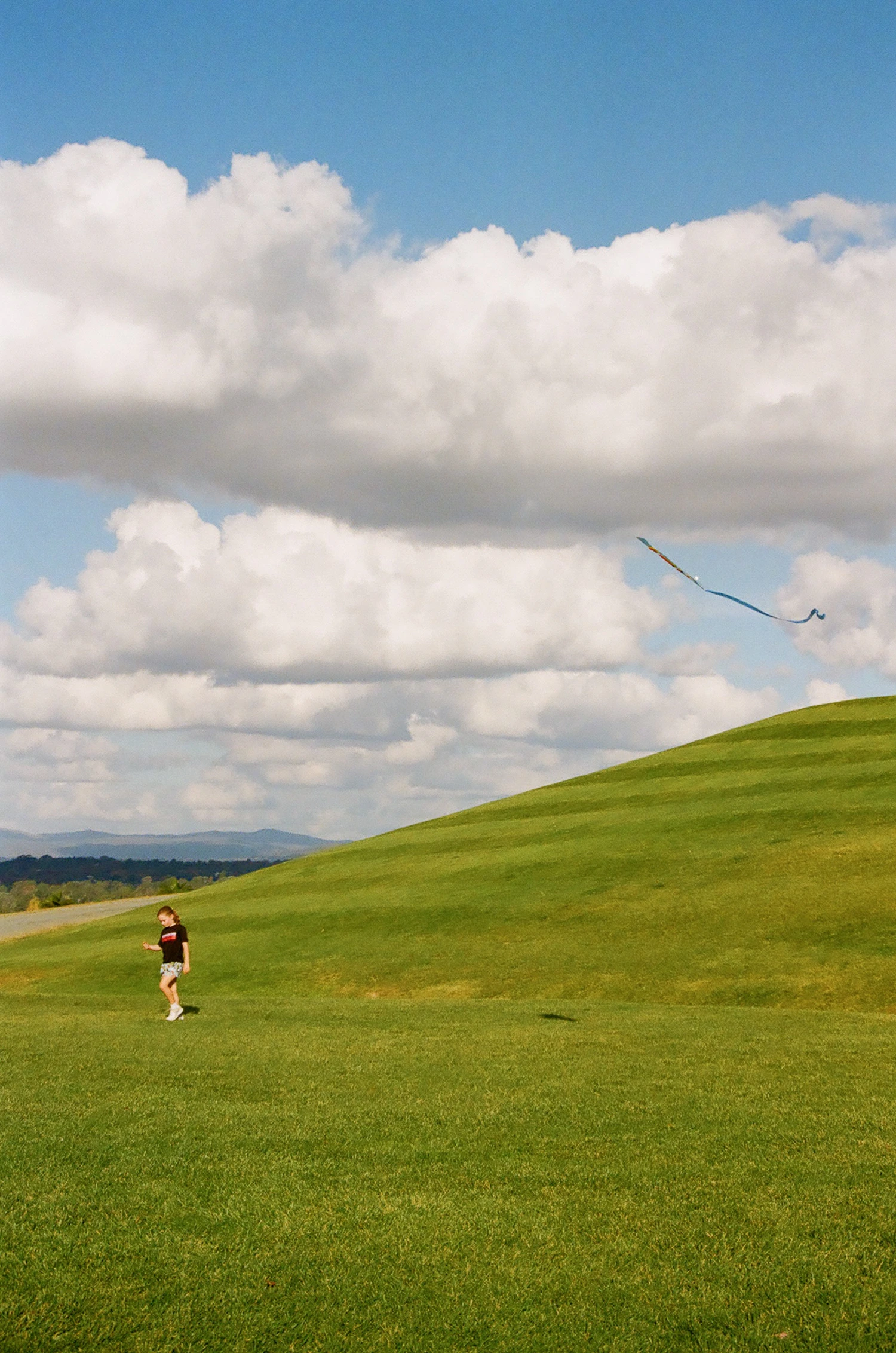 A child flying a kite on a grassy hill below a cloudy sky