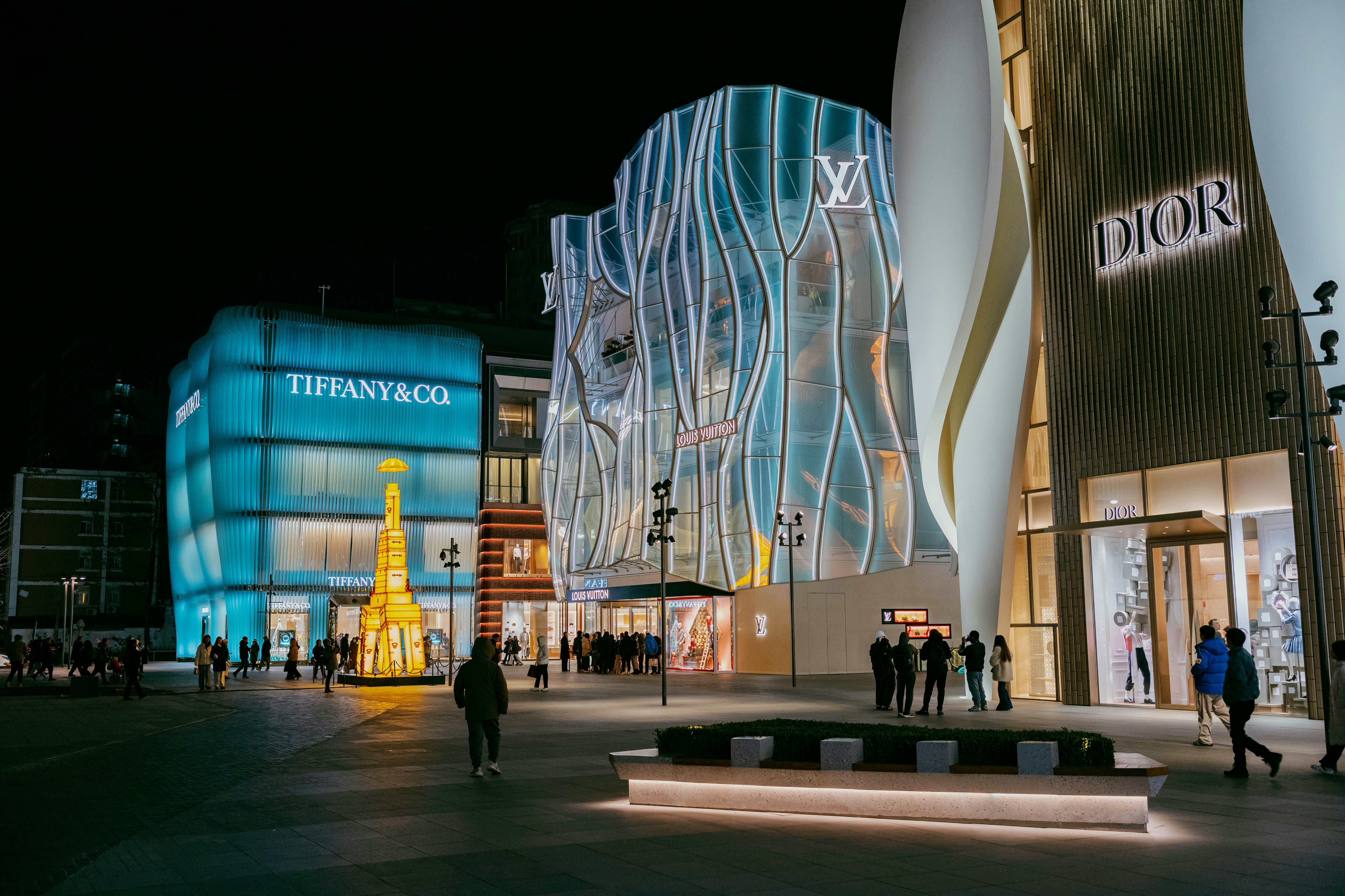 Luxury brand stores illuminated at night with people walking