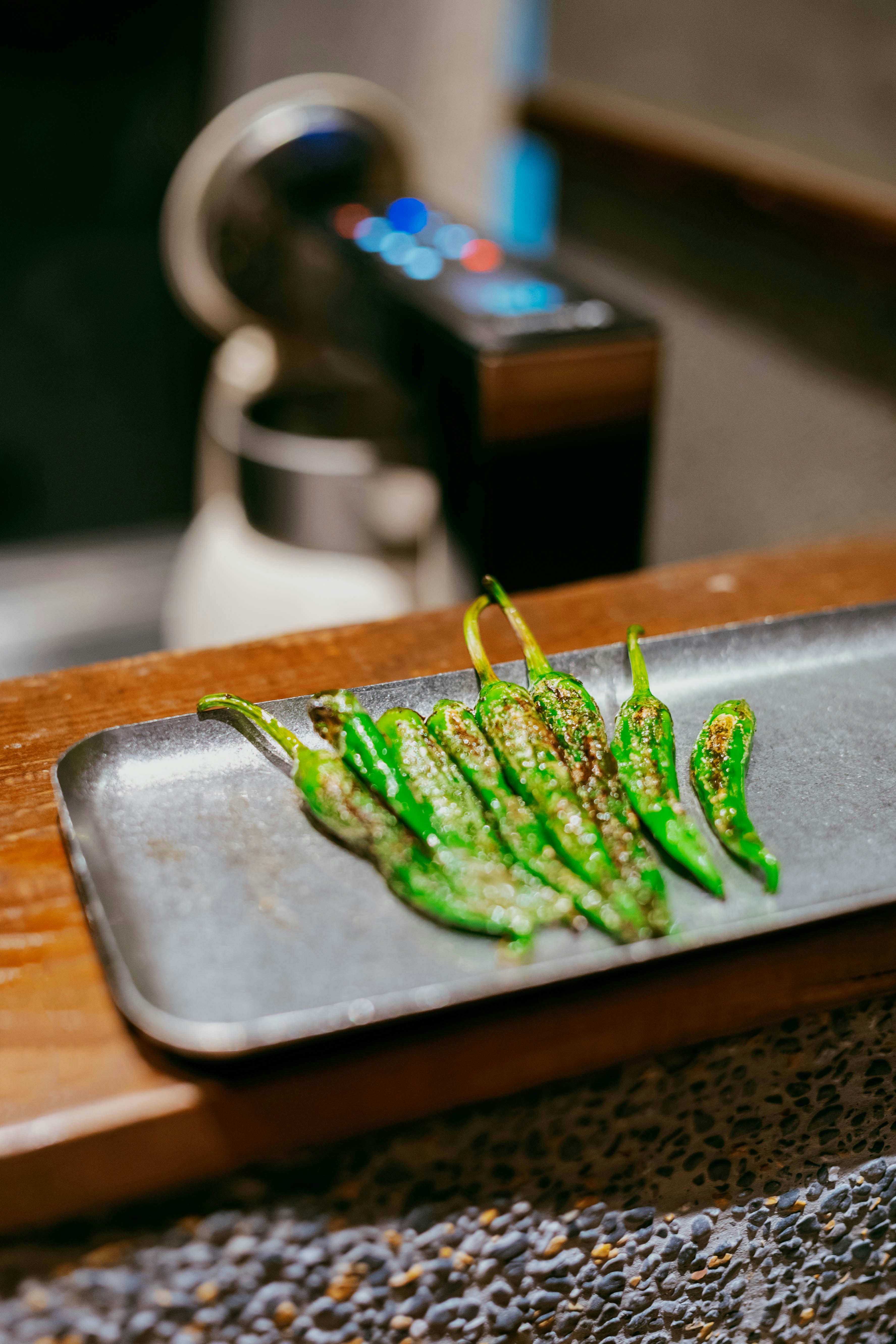 Grilled green peppers on a dark rectangular plate.