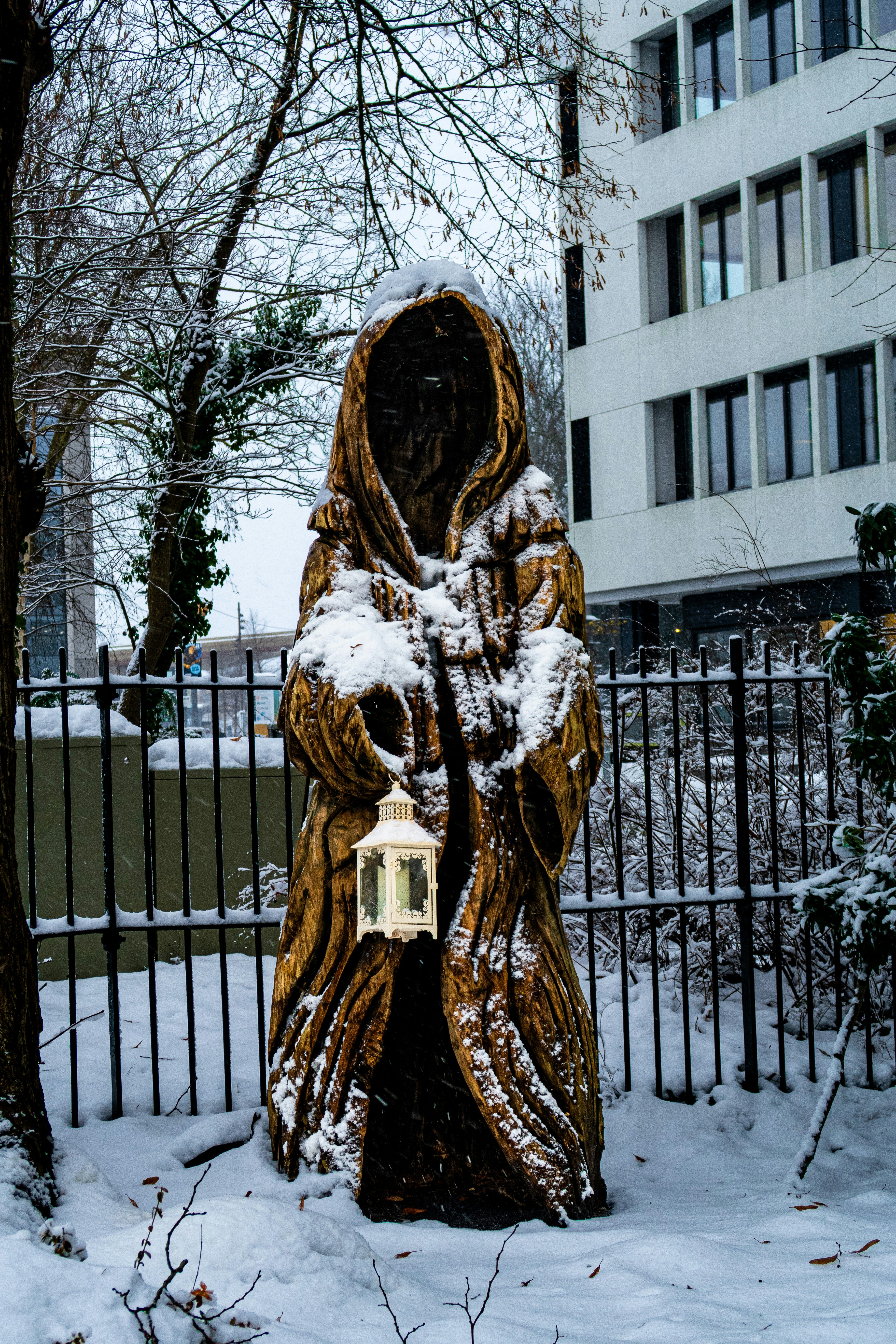 Wooden cloaked figure holding a lantern in snow