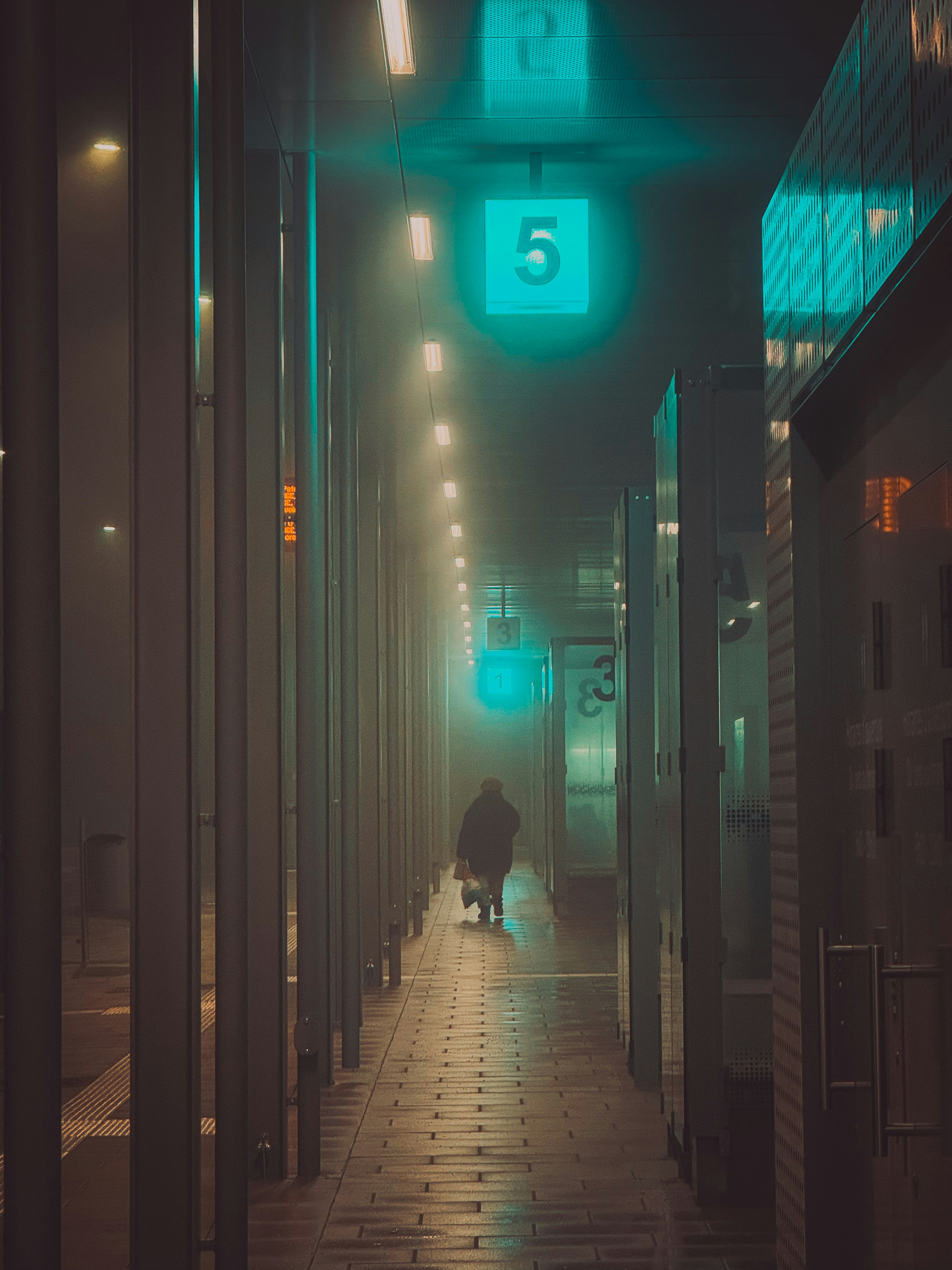 Person walks down foggy street at night with lights.