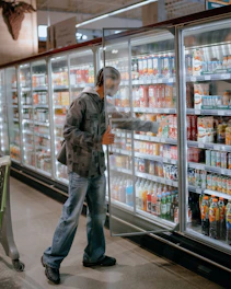 Man choosing drinks from a refrigerated grocery store display.