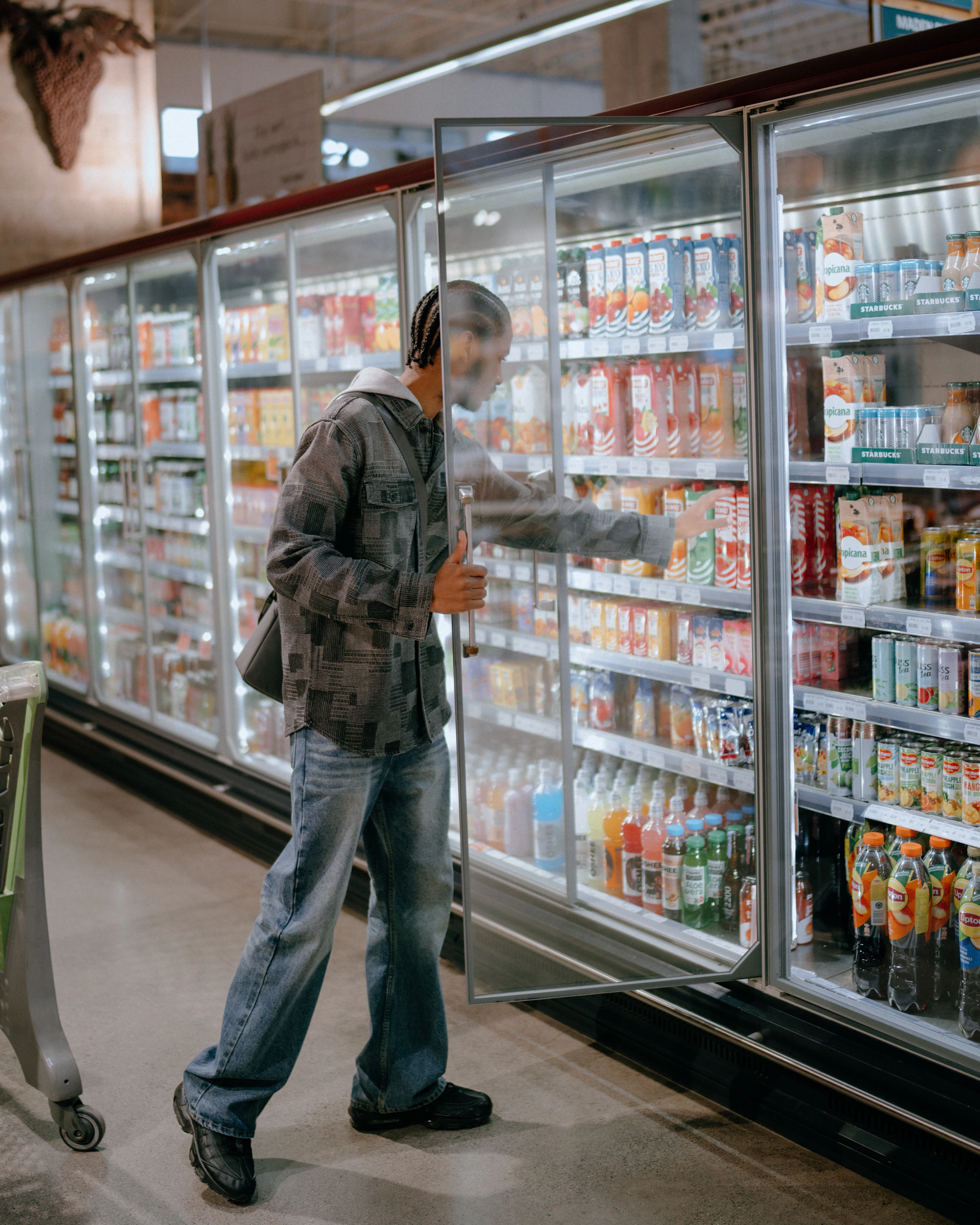 Man choosing drinks from a refrigerated grocery store display.