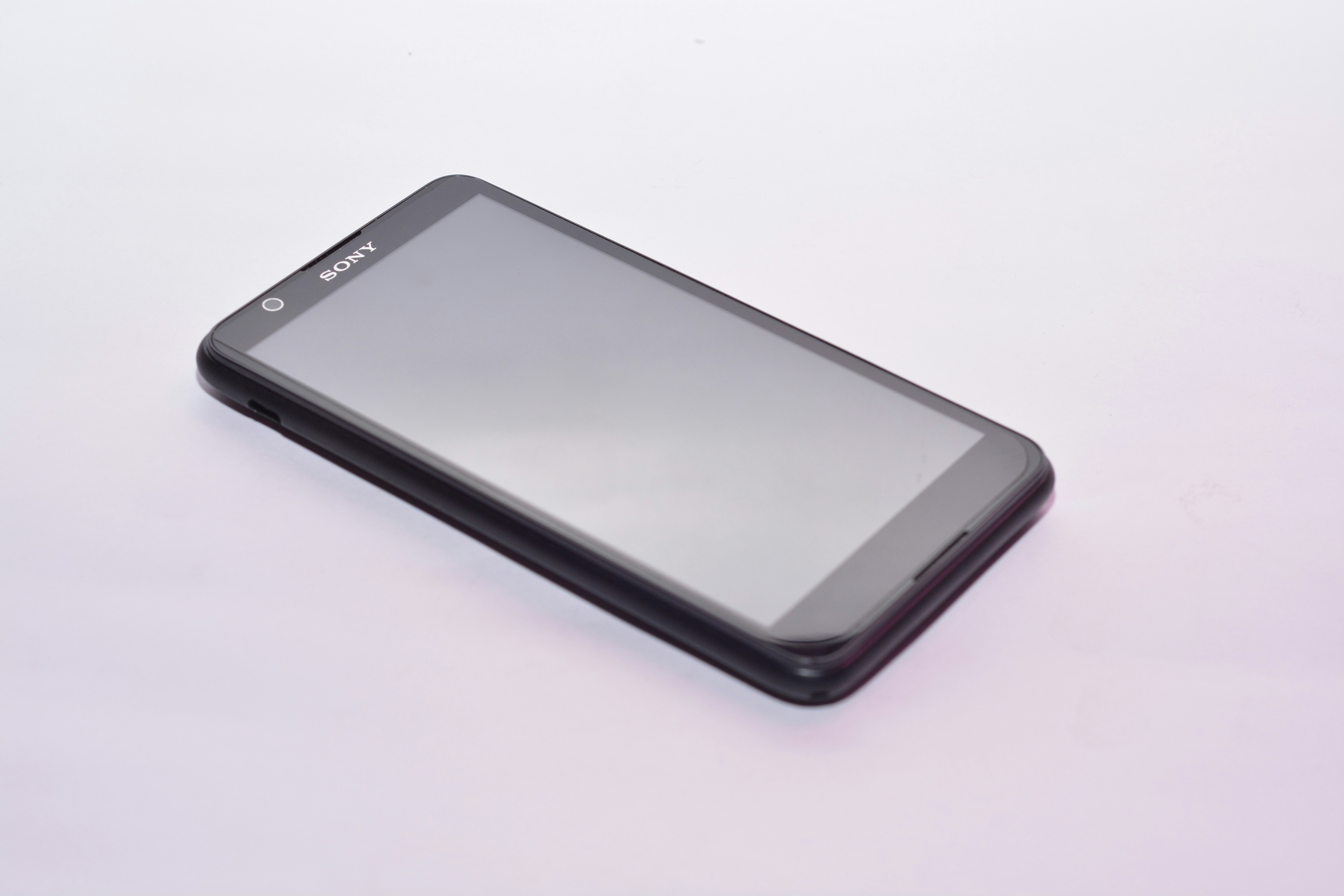 Un smartphone negro apoyado sobre una superficie blanca.