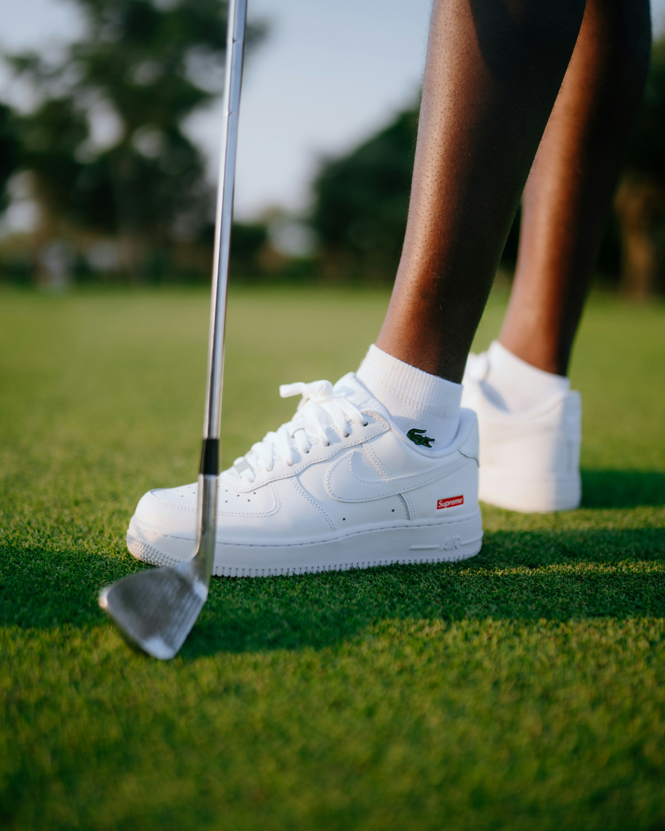 Golfer wearing white sneakers on green grass.