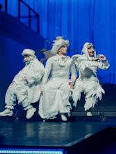 Three performers in white costumes on stage.